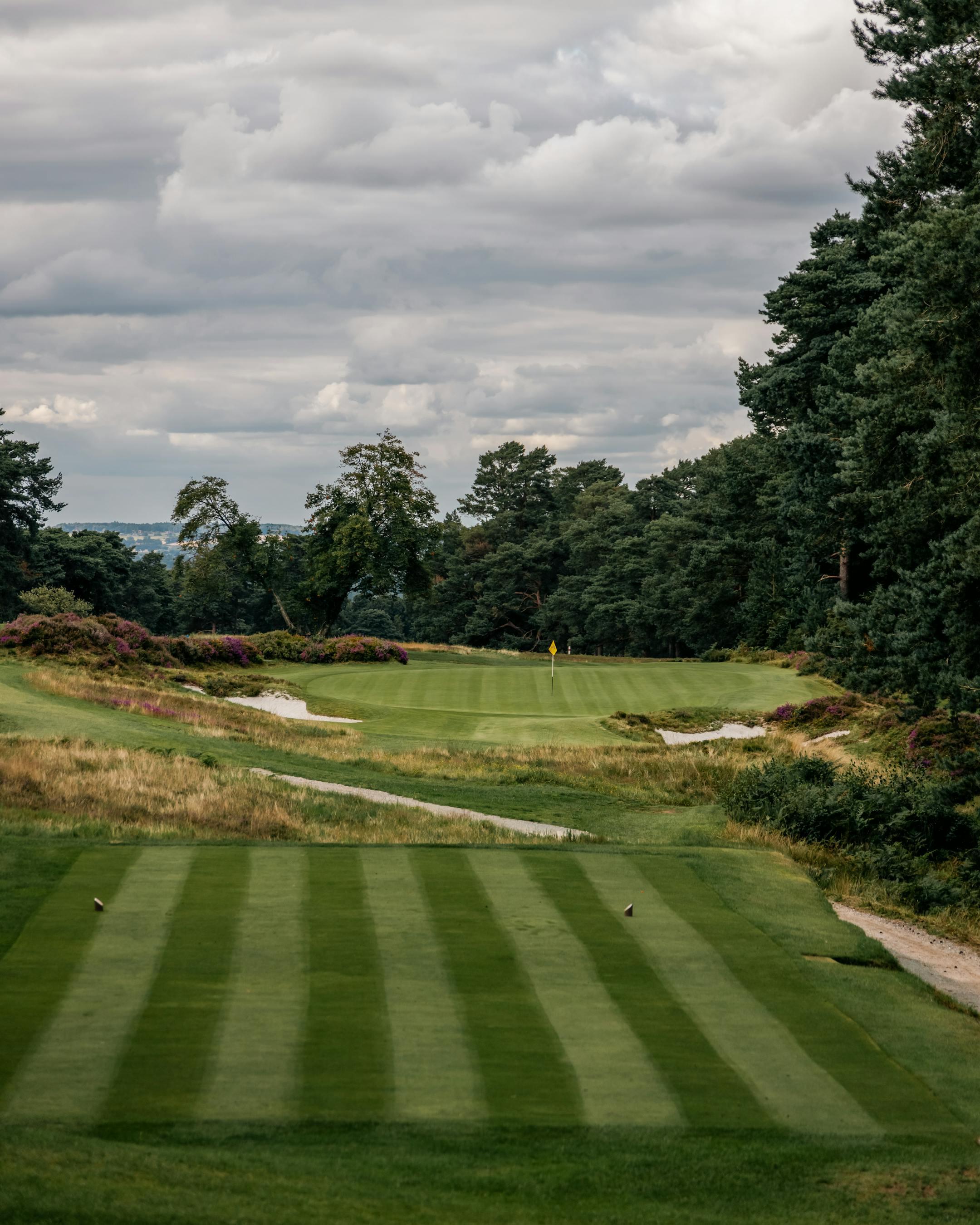 Scenic view of a lush green golf course in England set under a cloudy sky.