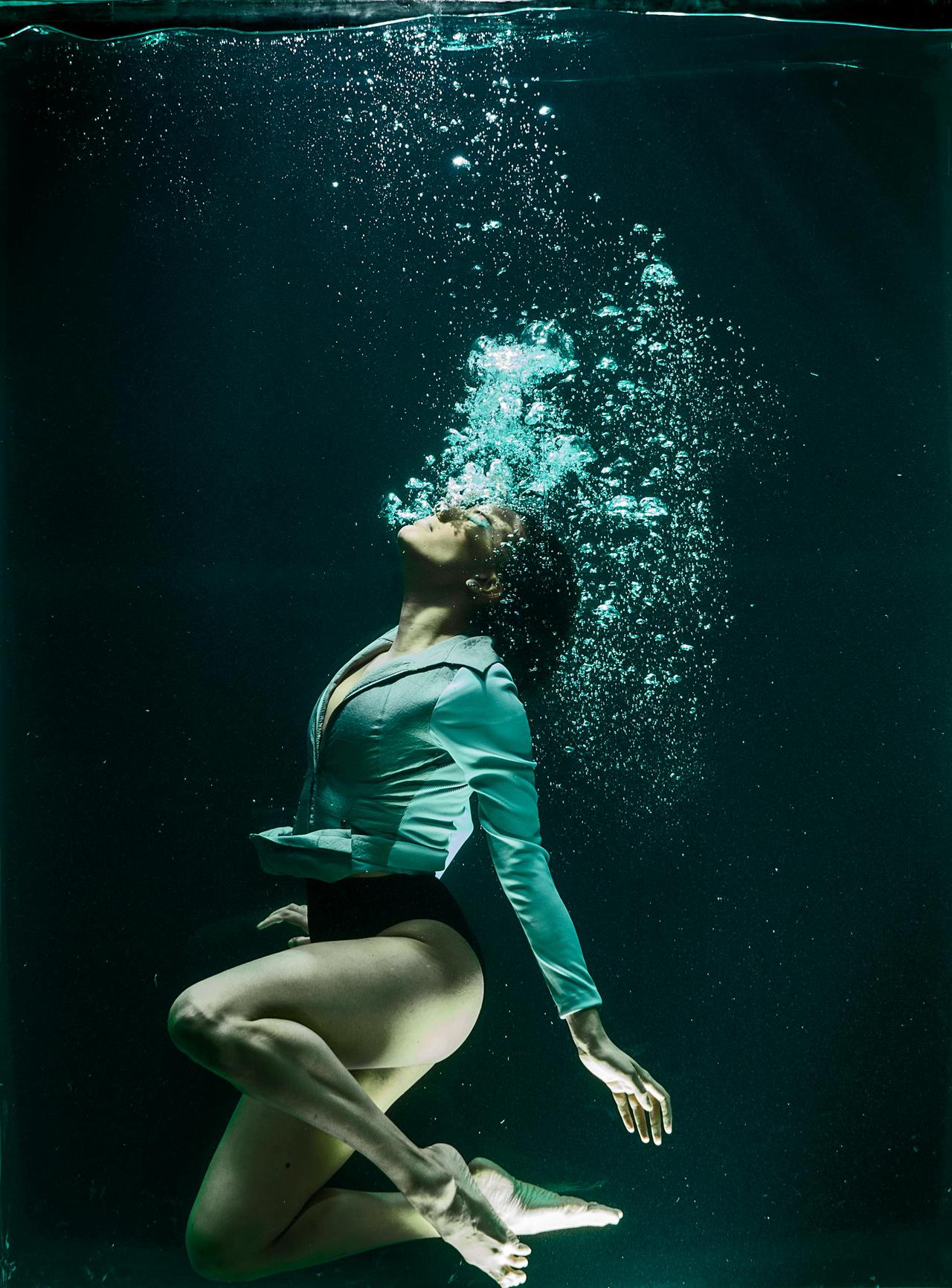 Dramatic photo of a woman diving underwater in stylish attire.