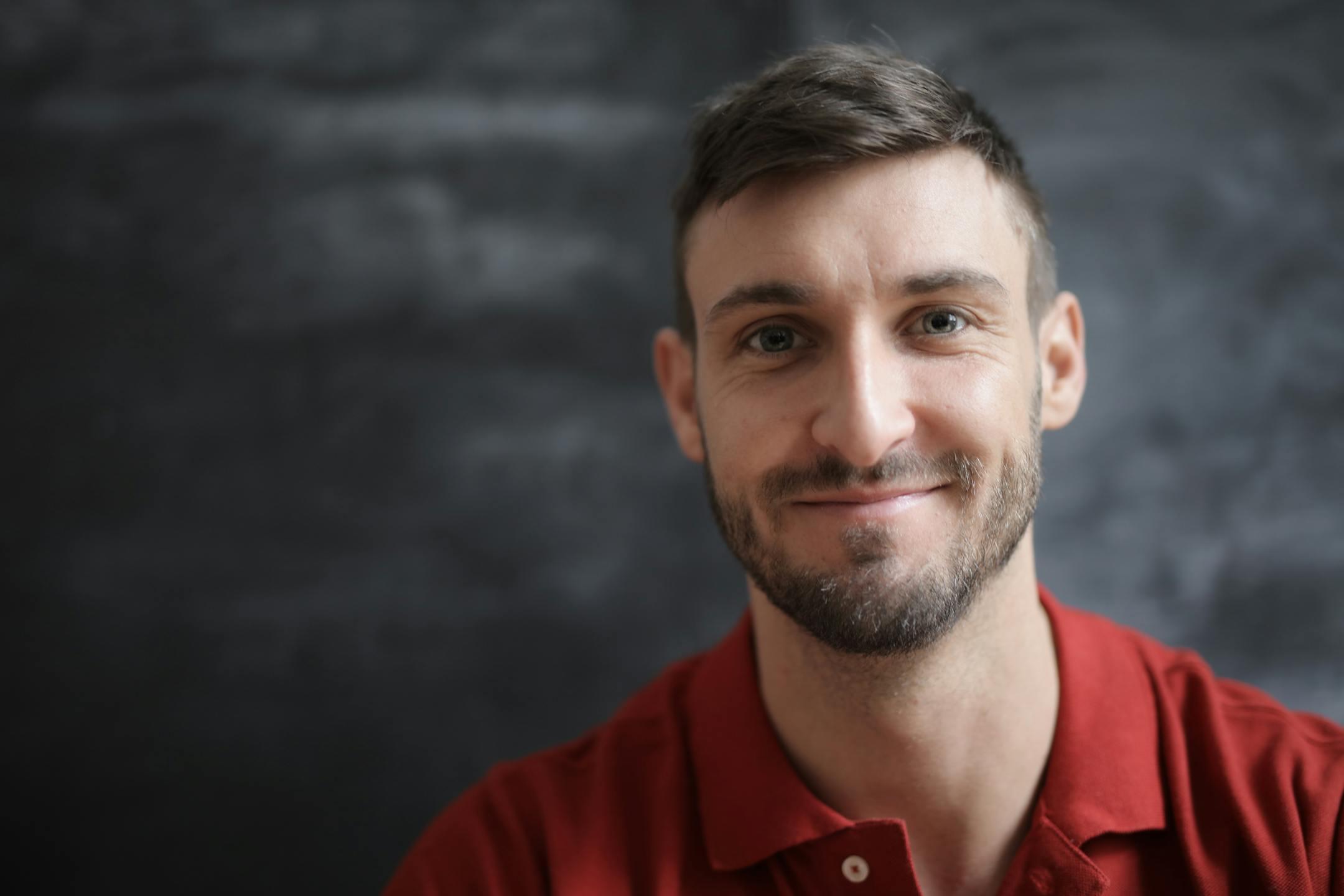 A smiling man in a red polo shirt poses for a portrait with a blurred background.