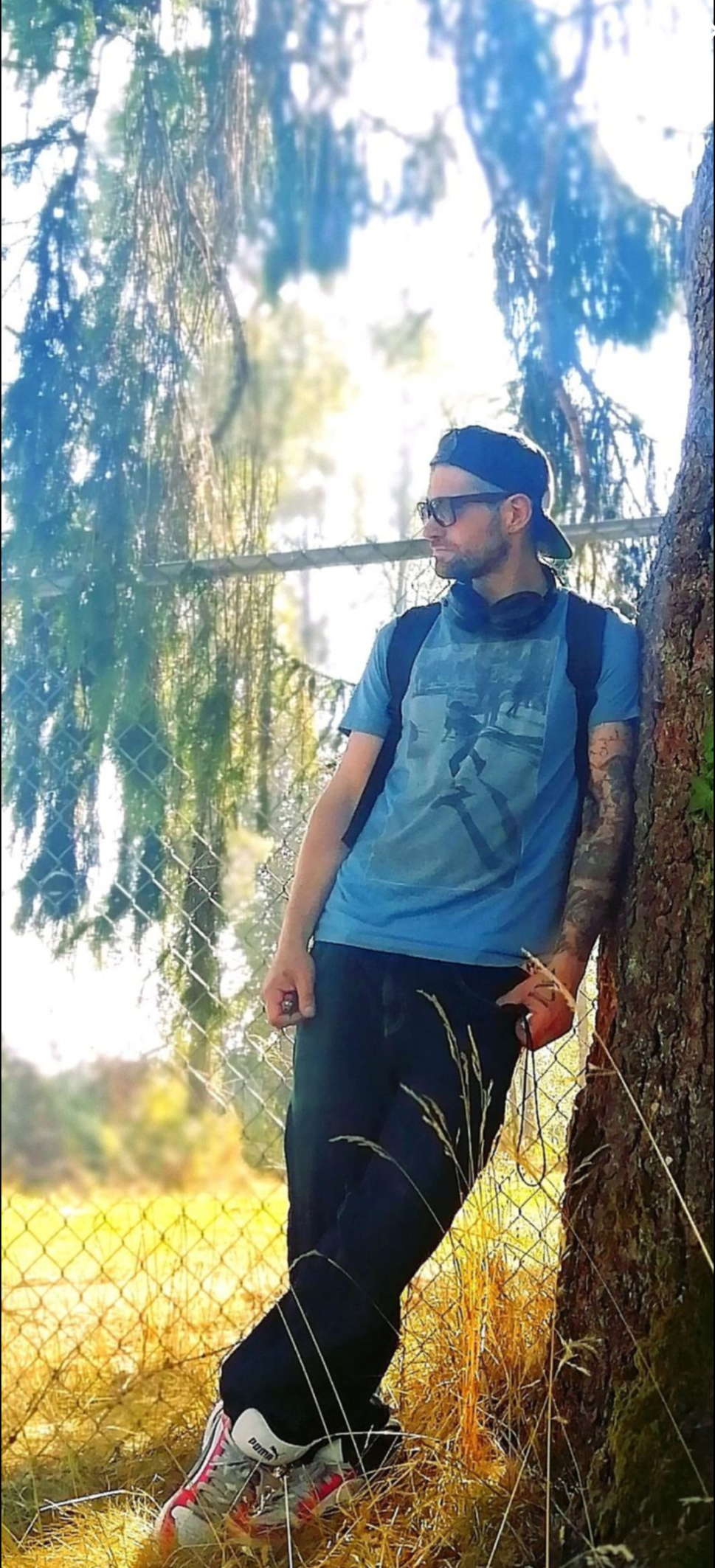 A young person sits quietly against a moss-covered tree trunk in a dim green forest, absorbed in thought, dappled light falling across the scene
