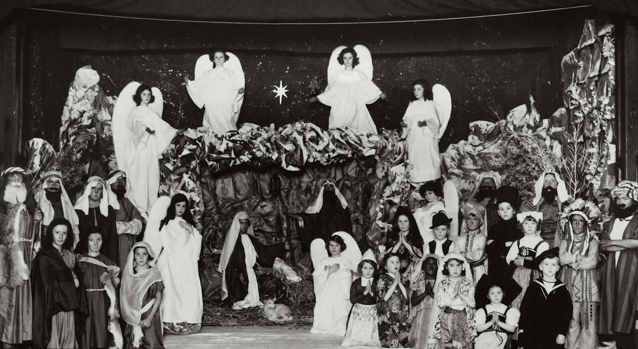 A historic black and white photograph of a children's nativity play featuring costumes and festive decorations.