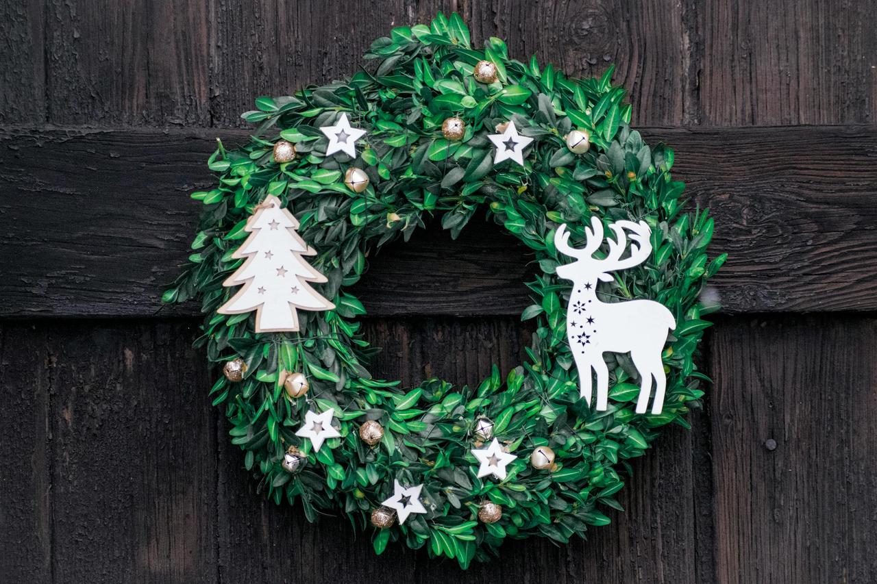 Beautiful green Christmas wreath with deer and tree decoration on a rustic wooden door.