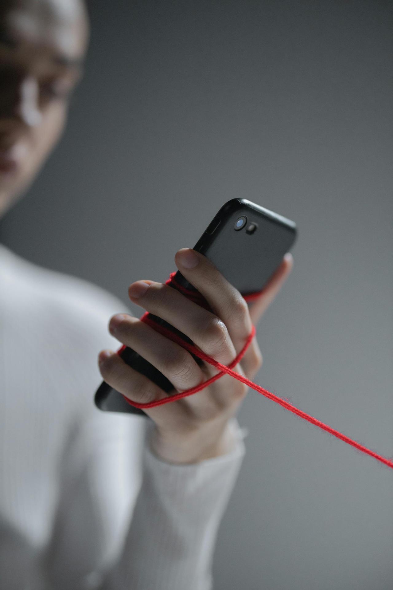 Close-up of a smartphone wrapped in red thread, symbolizing digital connection.