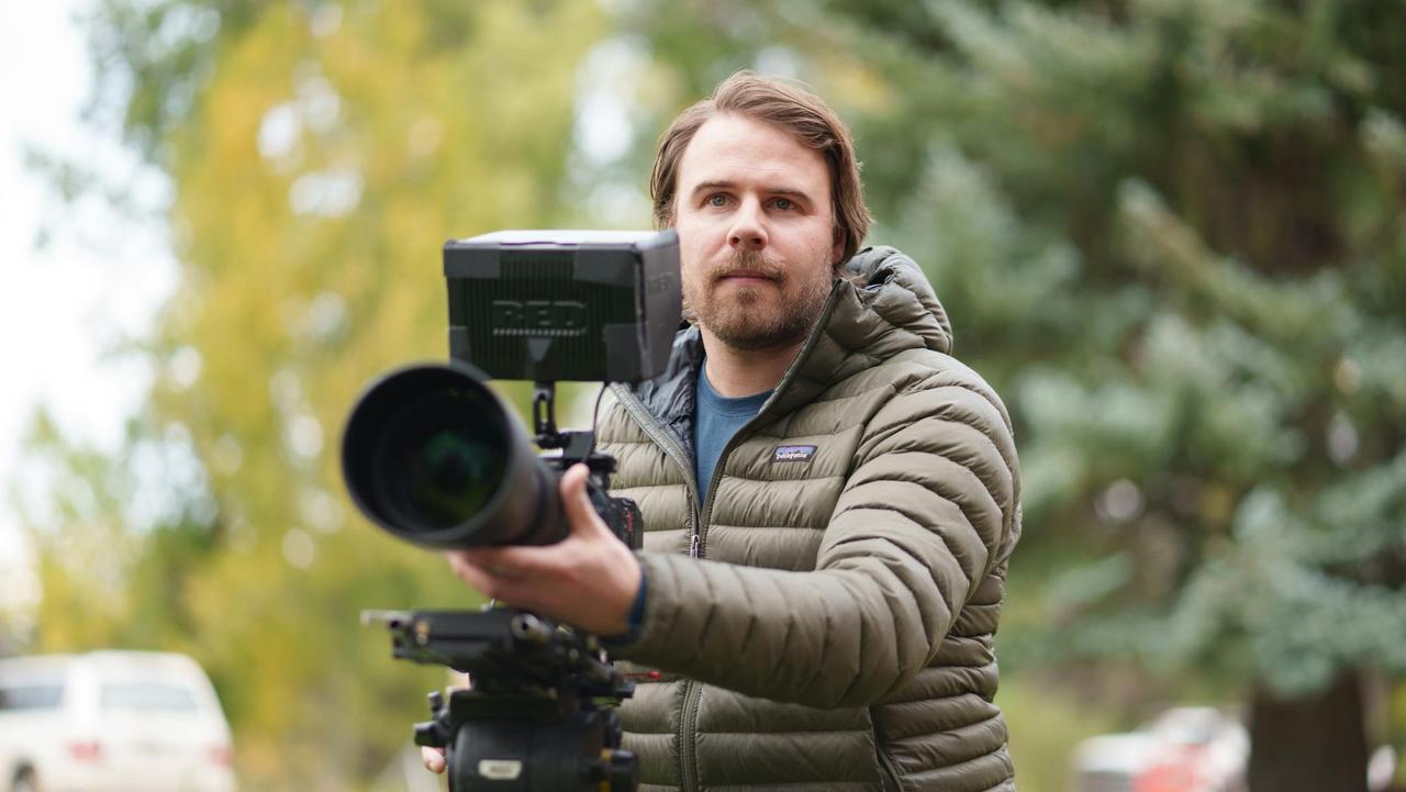 Male videographer shooting outdoors with professional camera equipment, wearing a warm jacket.