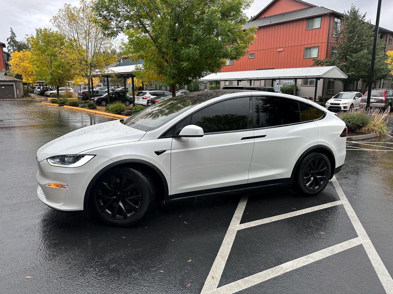 A sleek white electric SUV with tinted windows is parked in a Seattle neighborhood on a rainy fall day.