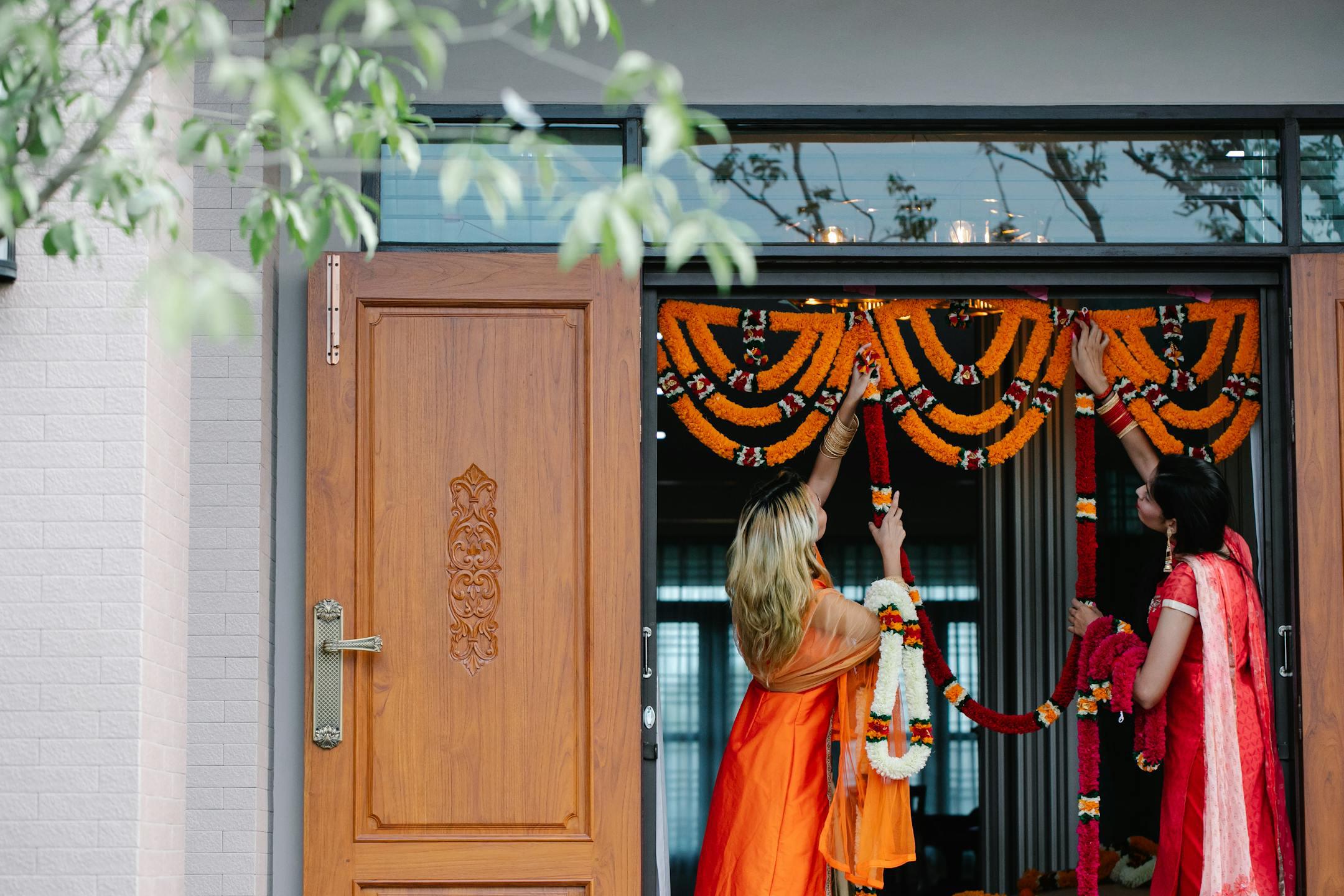 Colorful floral garlands being arranged for a festive ceremony at a wooden doorway.