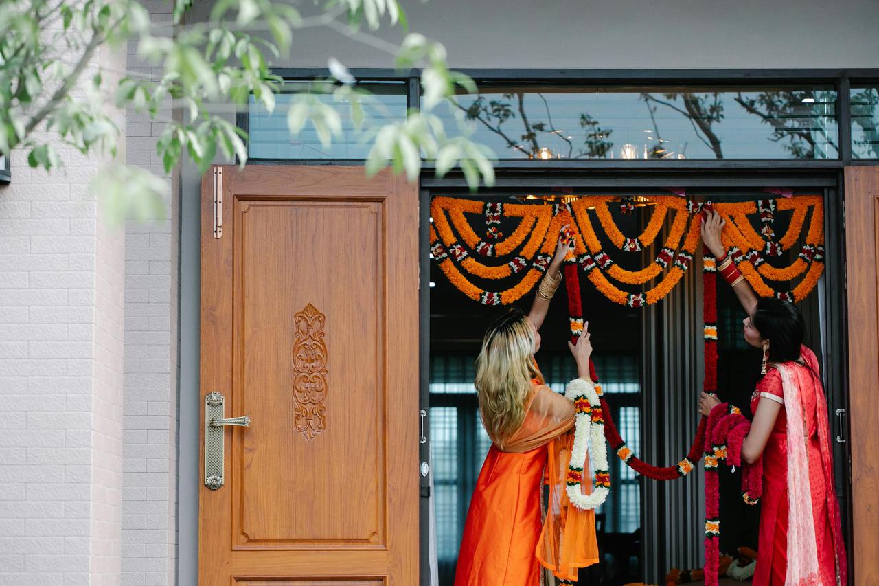 Colorful floral garlands being arranged for a festive ceremony at a wooden doorway.