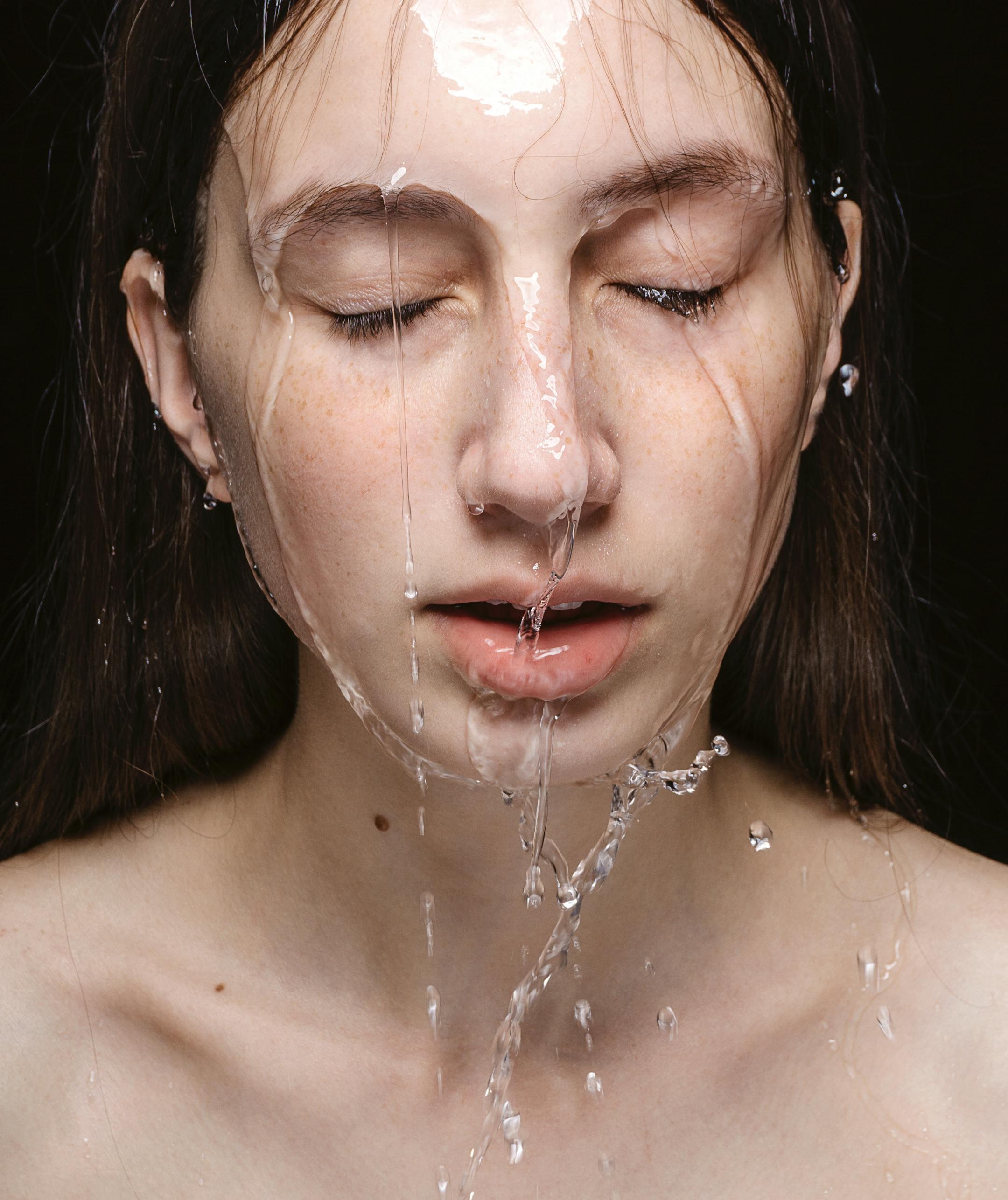 Serene close-up portrait of a woman with water dripping on her face, conveying calm and tranquility.