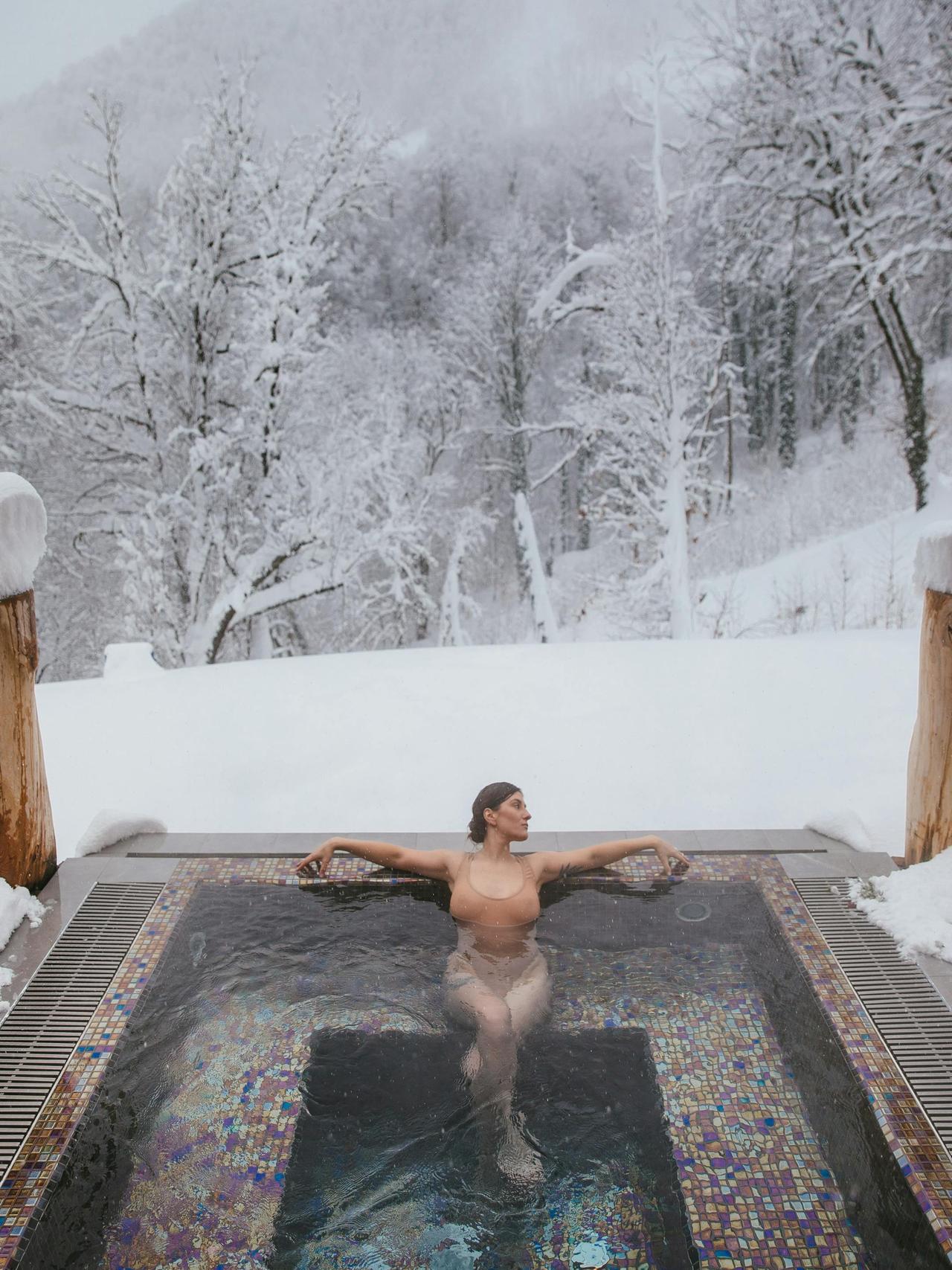 A woman enjoying a hot tub amidst a snowy forest landscape, creating a serene winter retreat.