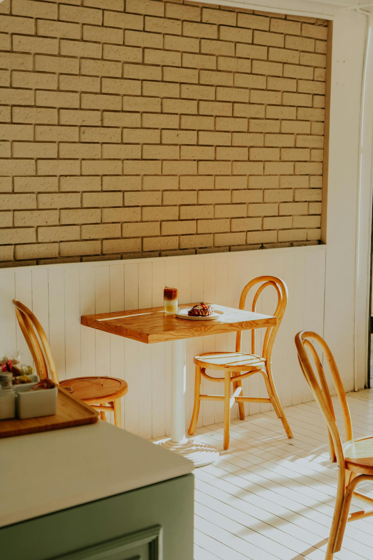 Sunlit café interior with wooden chairs and table against a brick wall, creating a warm ambiance.