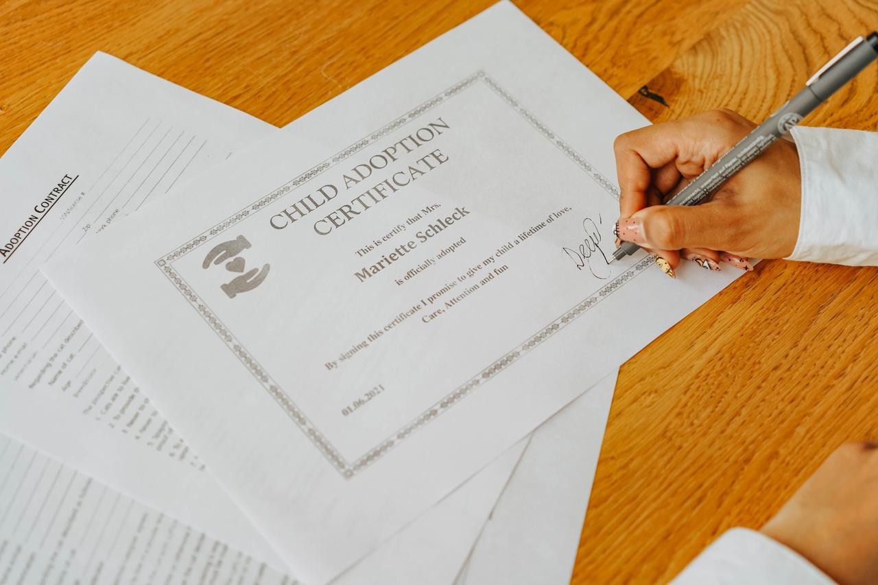 Close-up view of a hand signing an official child adoption certificate document.