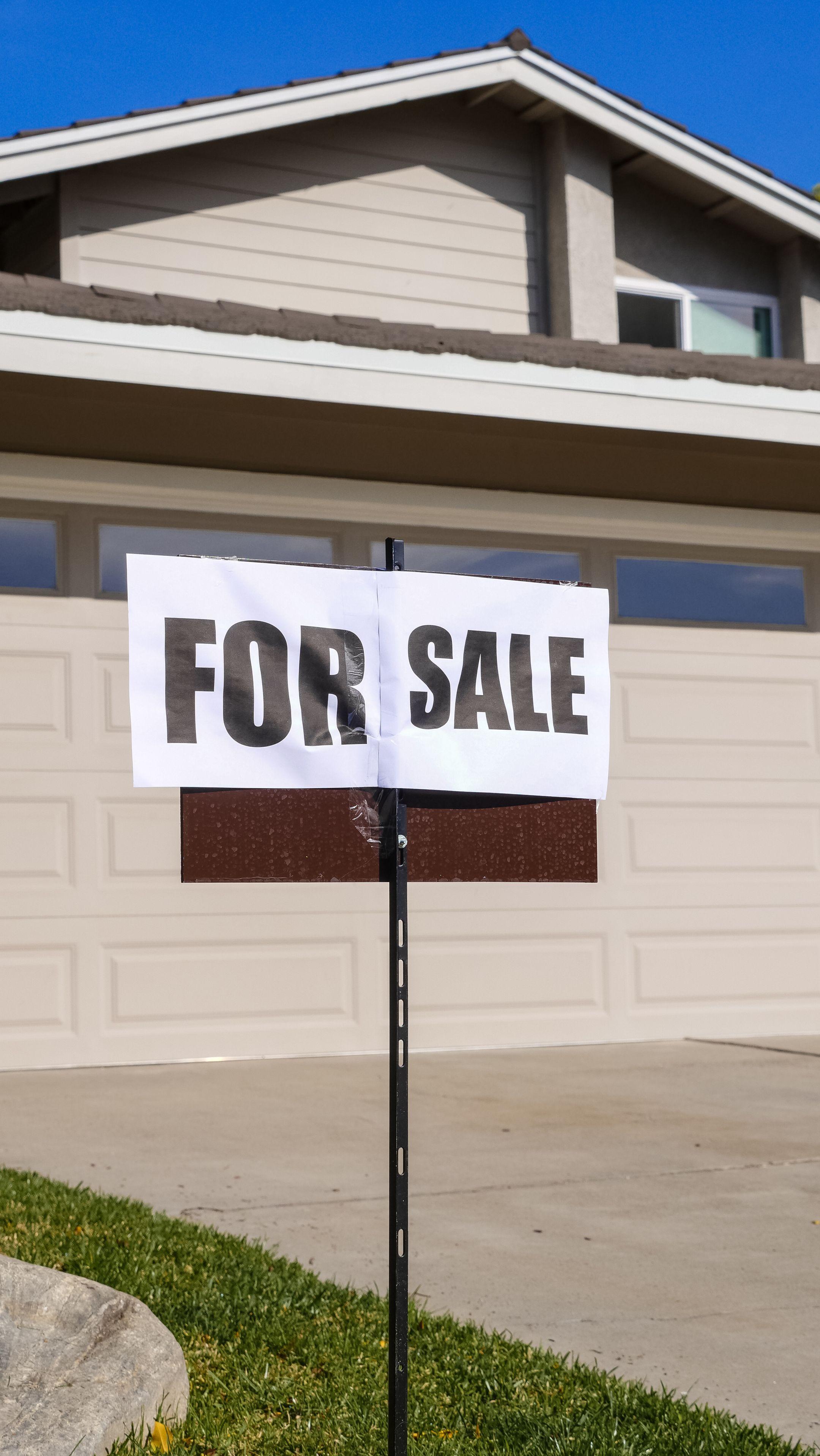 A modern suburban house with a prominent 'For Sale' sign in the front yard, ideal for real estate listings.