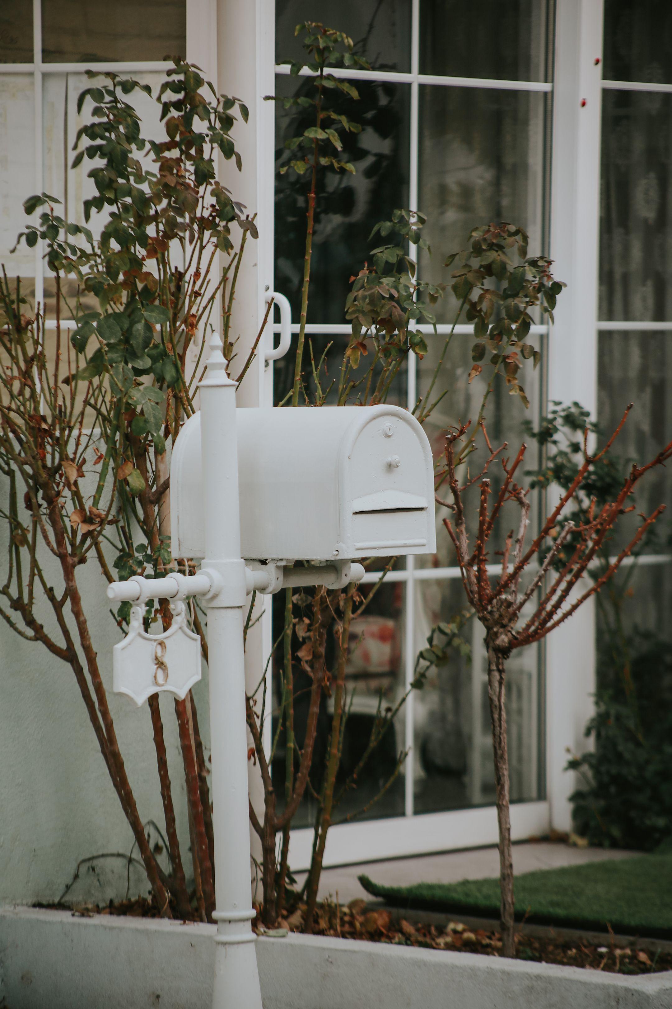 A classic white mailbox in front of a cozy house with bare shrubs, adding a rustic charm to the urban setting.