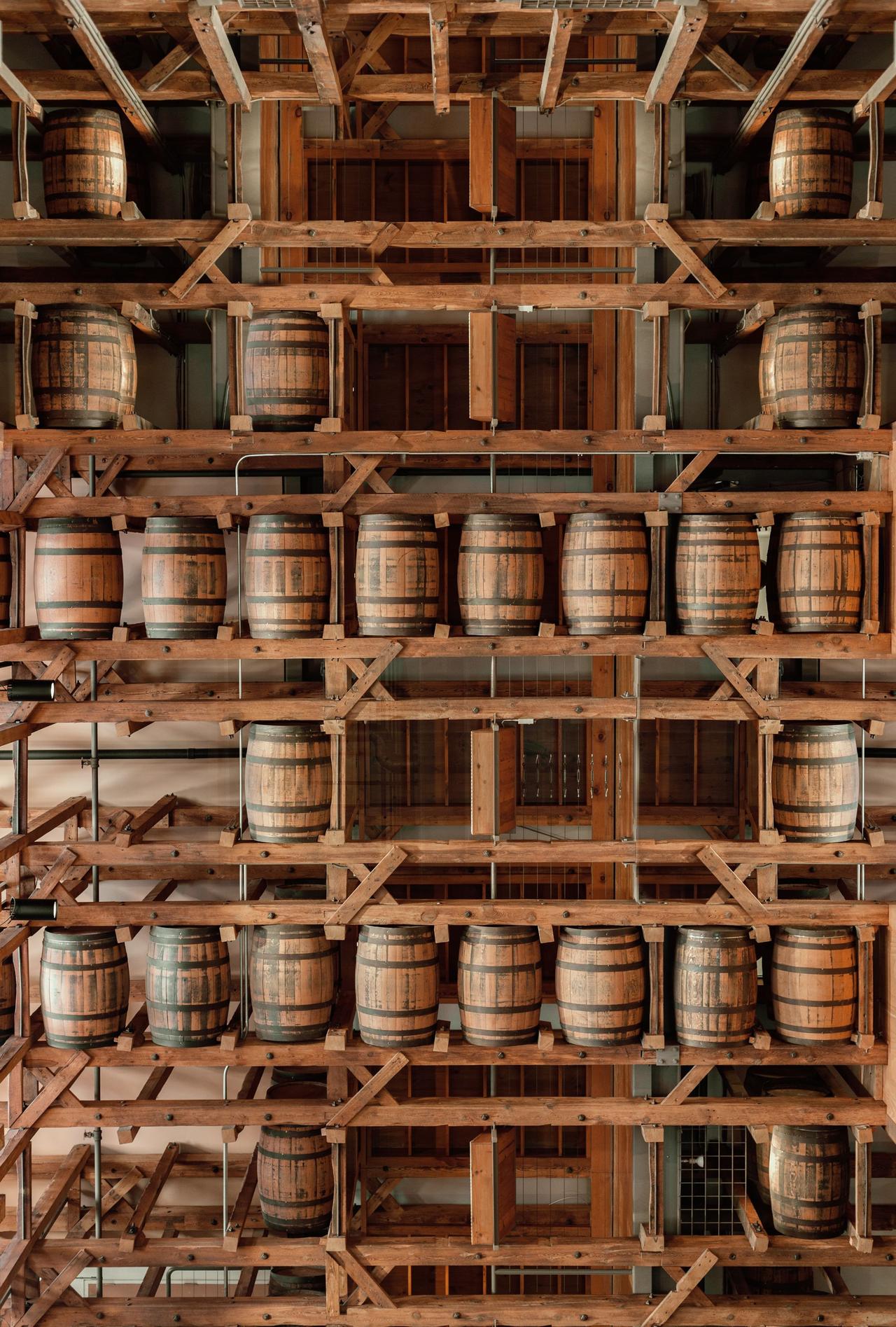 Vertical view of wooden barrels in a distillery storage with wooden shelves.