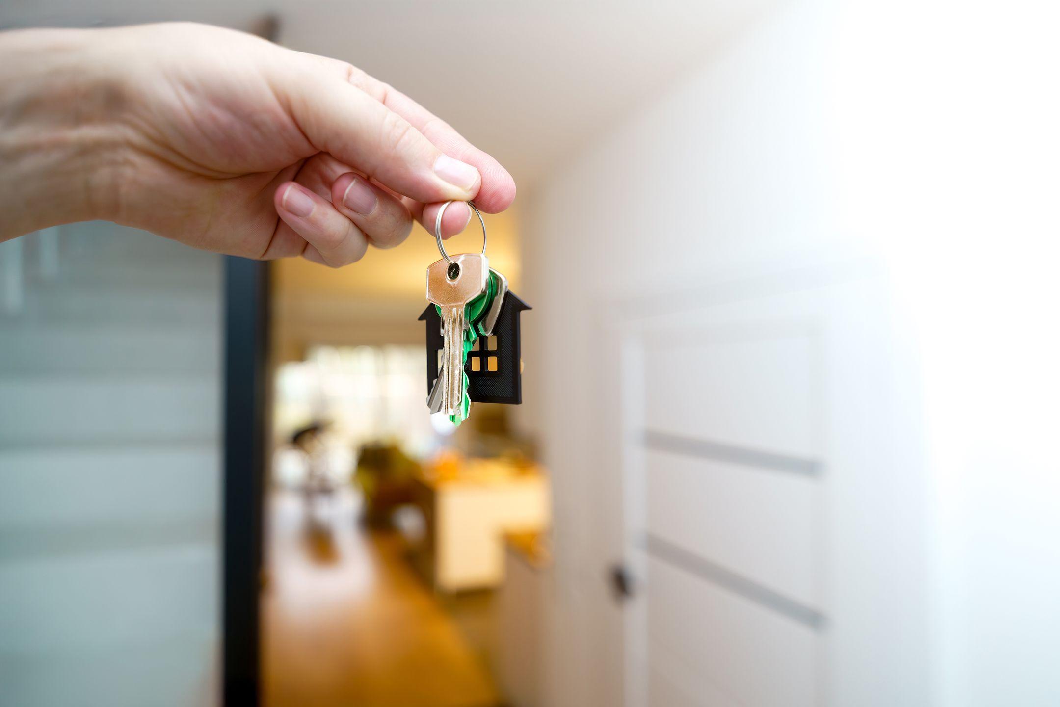 A hand holding house keys inside a modern apartment, symbolizing new property ownership or rental.