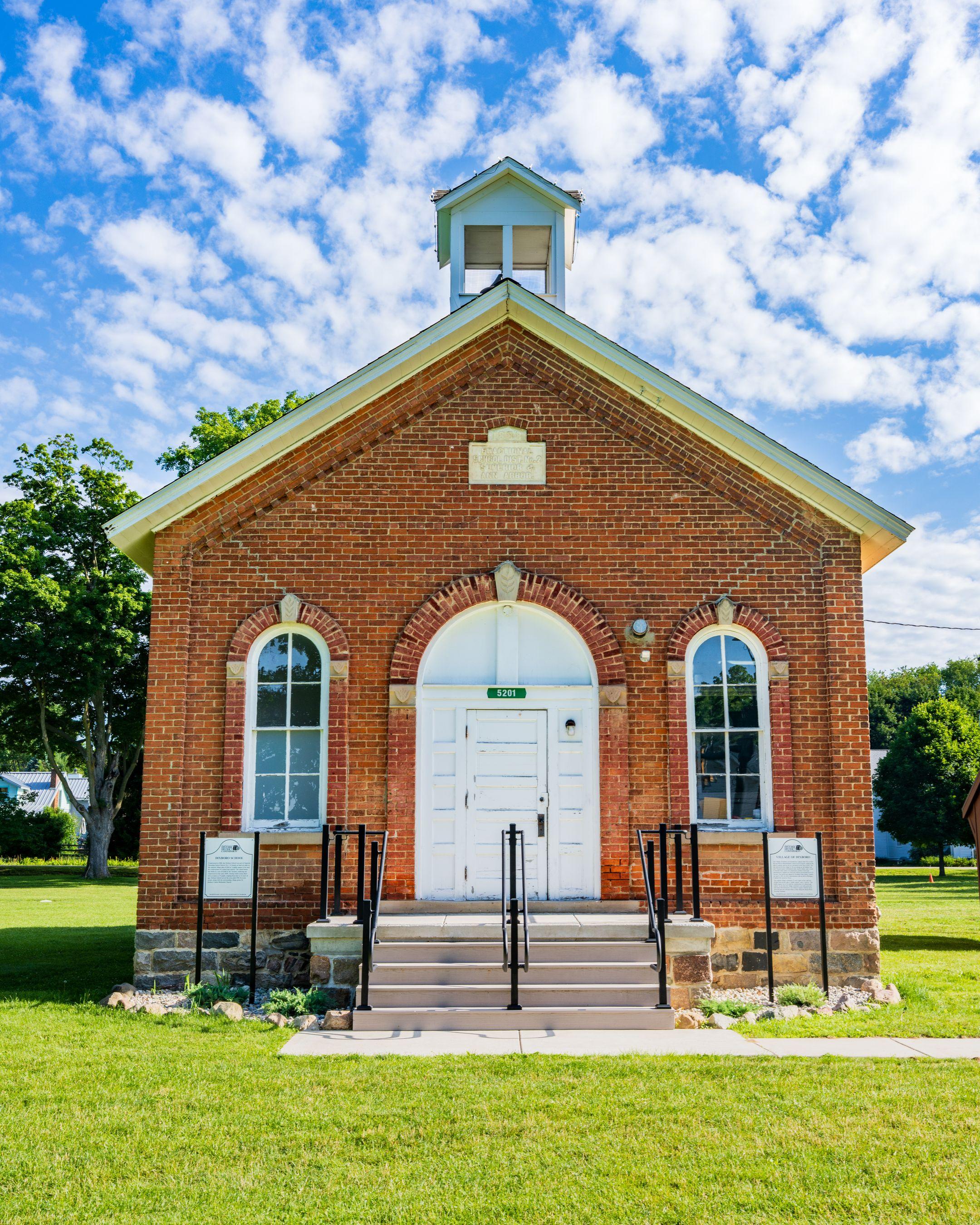 Front view of a historic brick schoolhouse under a bright blue sky in Michigan.