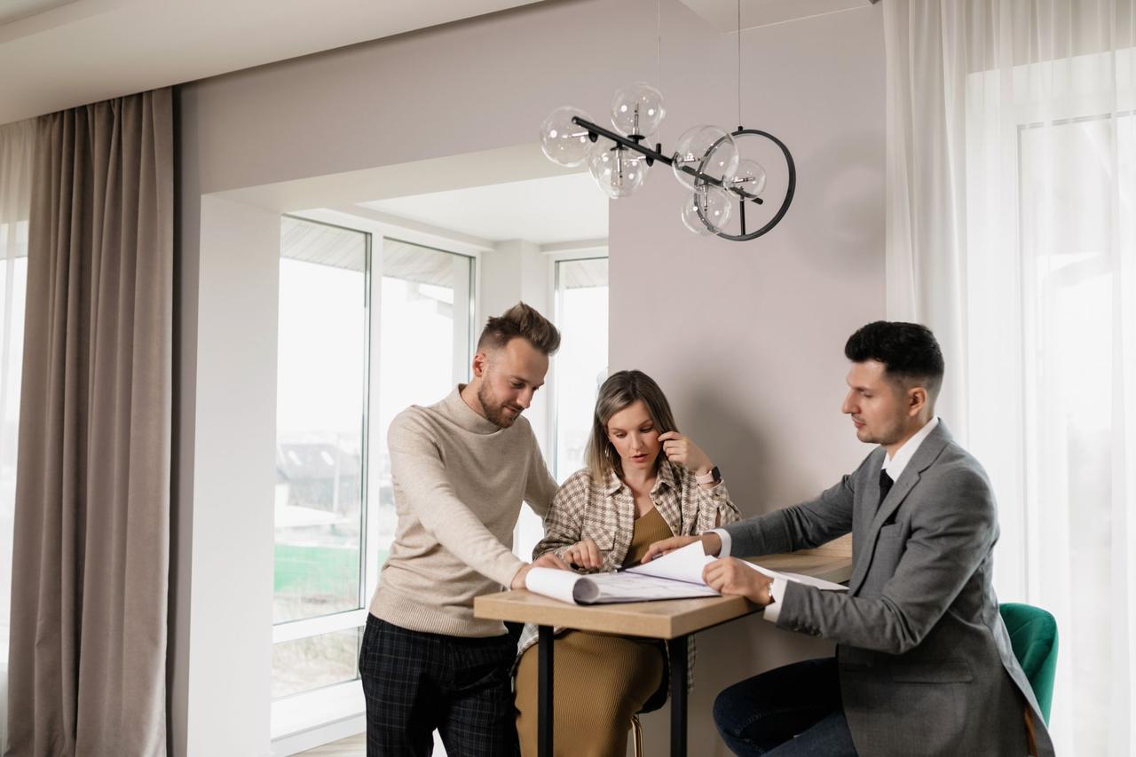A couple consults with a real estate agent in a modern indoor setting, reviewing property documents.