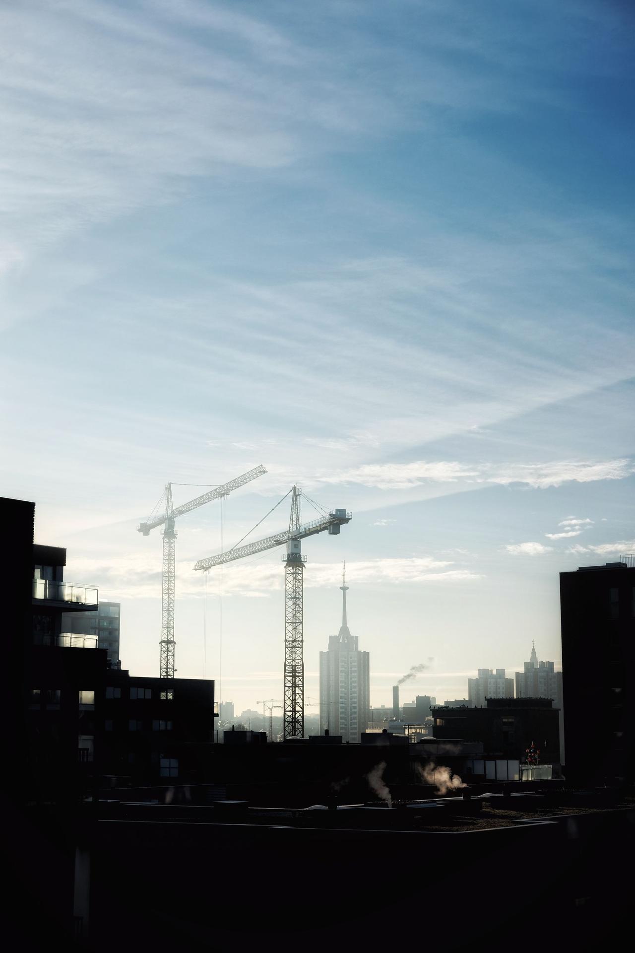 Silhouette of city skyline with construction cranes against a clear morning sky.