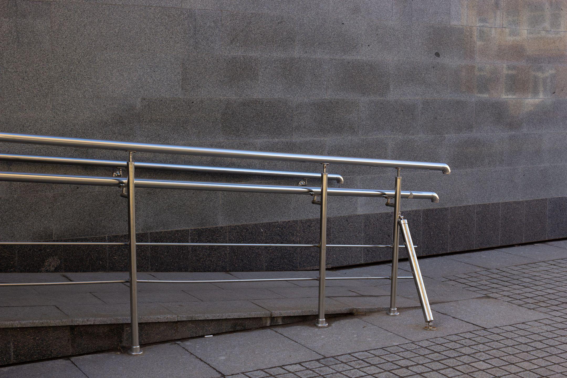Close-up of a metal handrail and concrete ramp for accessibility in an urban setting.