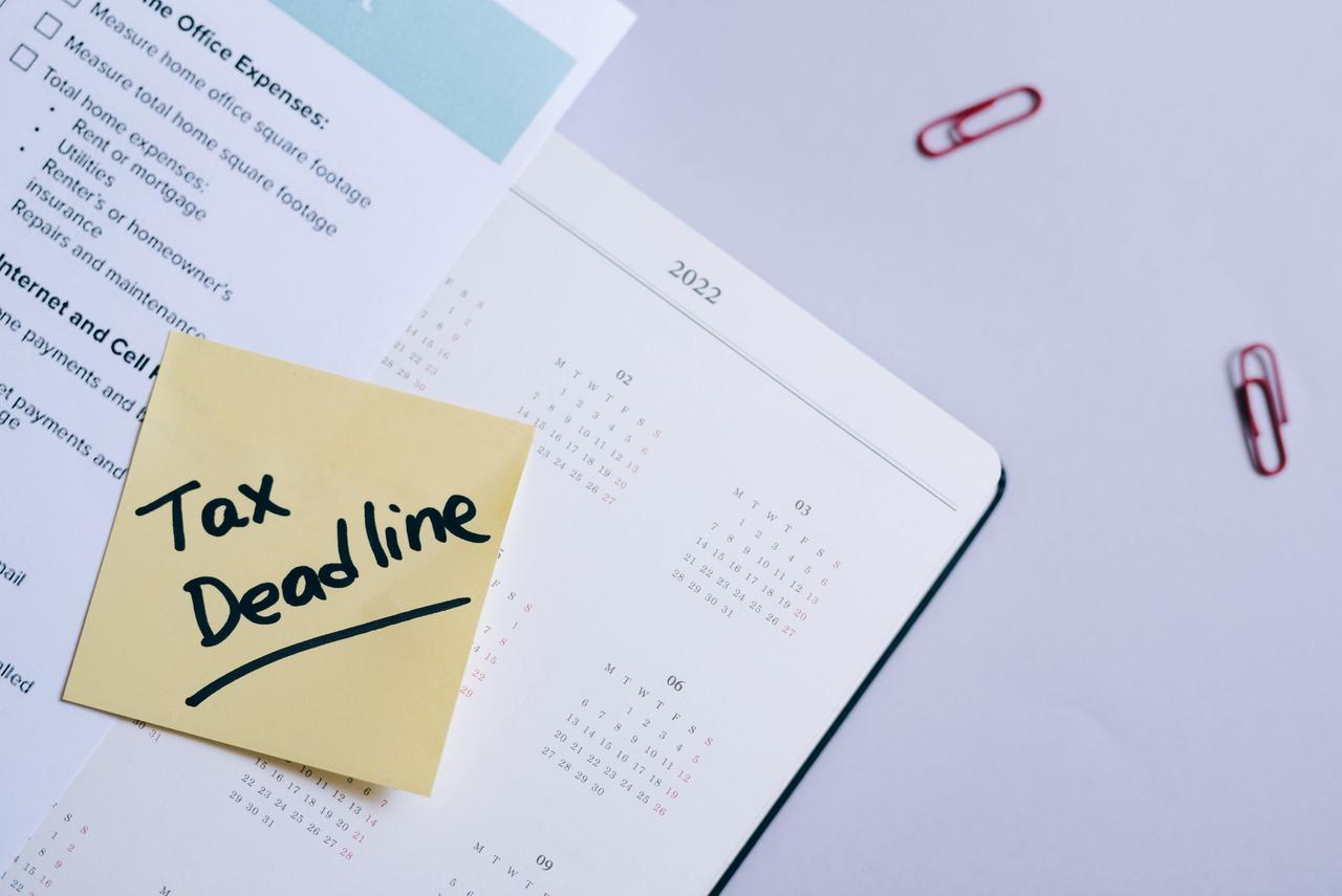 A sticky note highlights tax deadline on a calendar alongside documents, emphasizing financial planning.