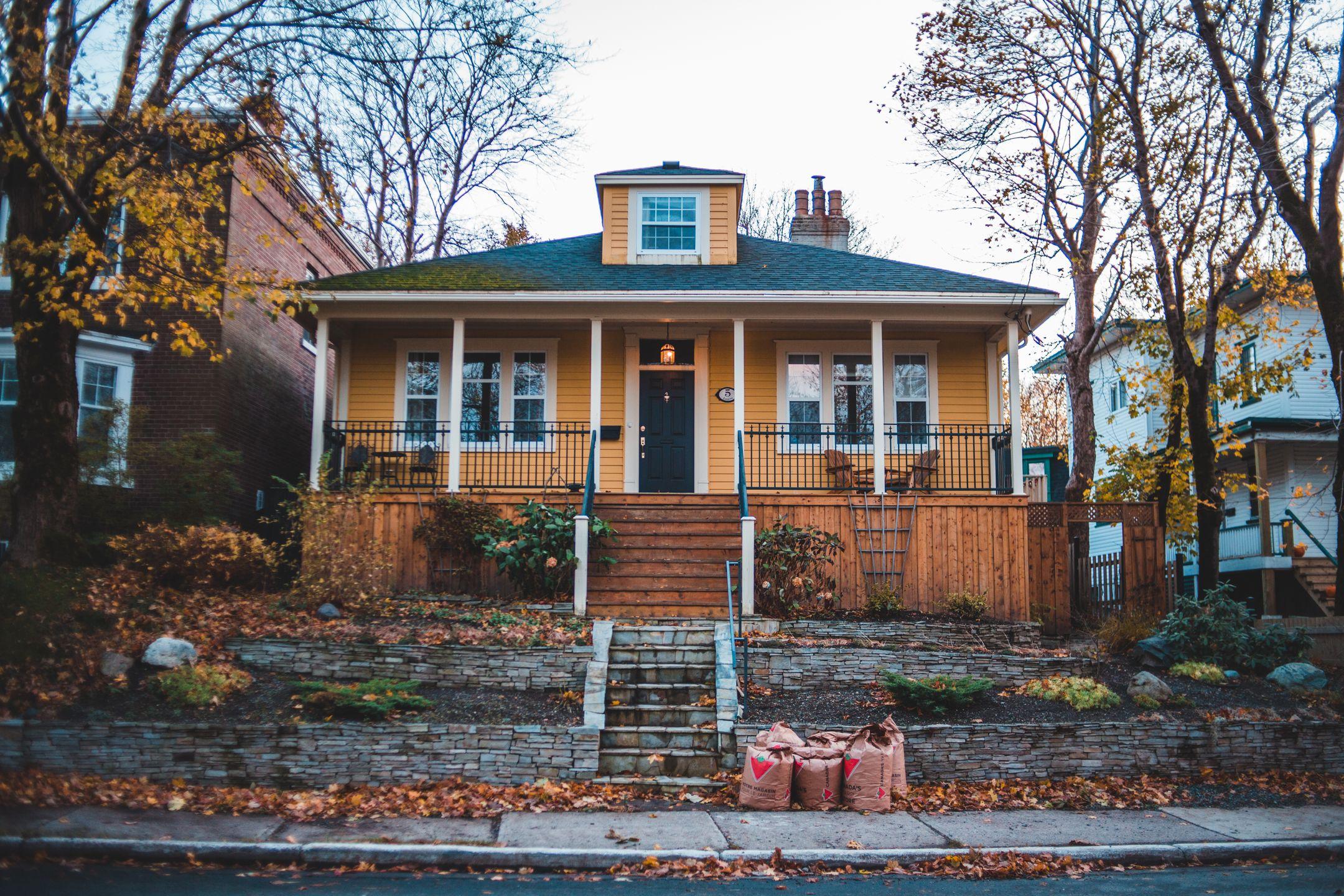 Cozy yellow bungalow surrounded by autumn leaves in a quiet suburban neighborhood.