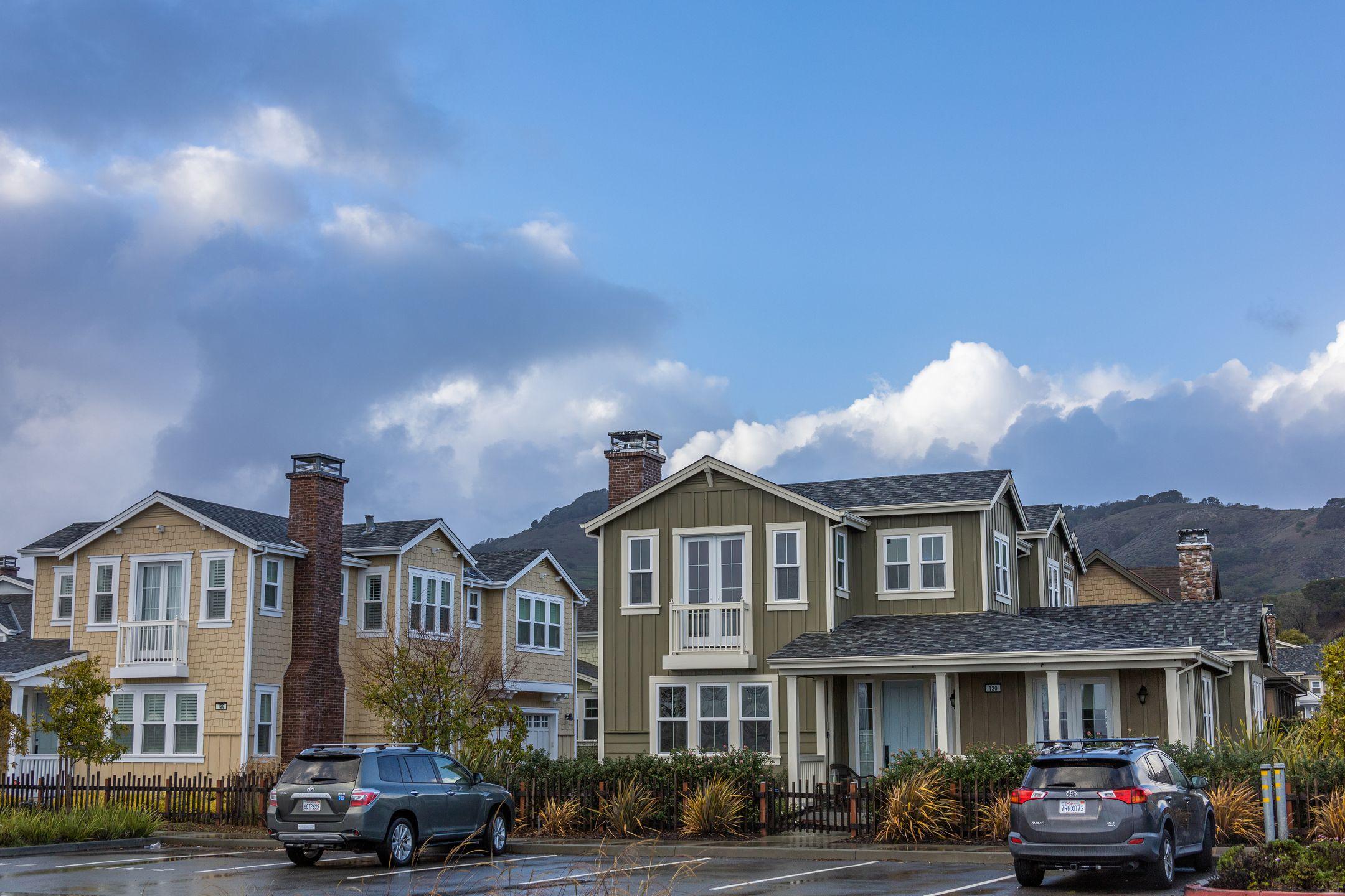 Picturesque suburban neighborhood with modern houses and parked cars under a partly cloudy sky.