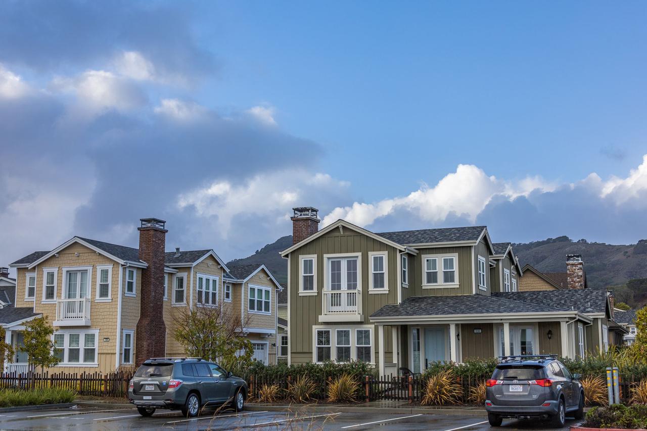 Picturesque suburban neighborhood with modern houses and parked cars under a partly cloudy sky.