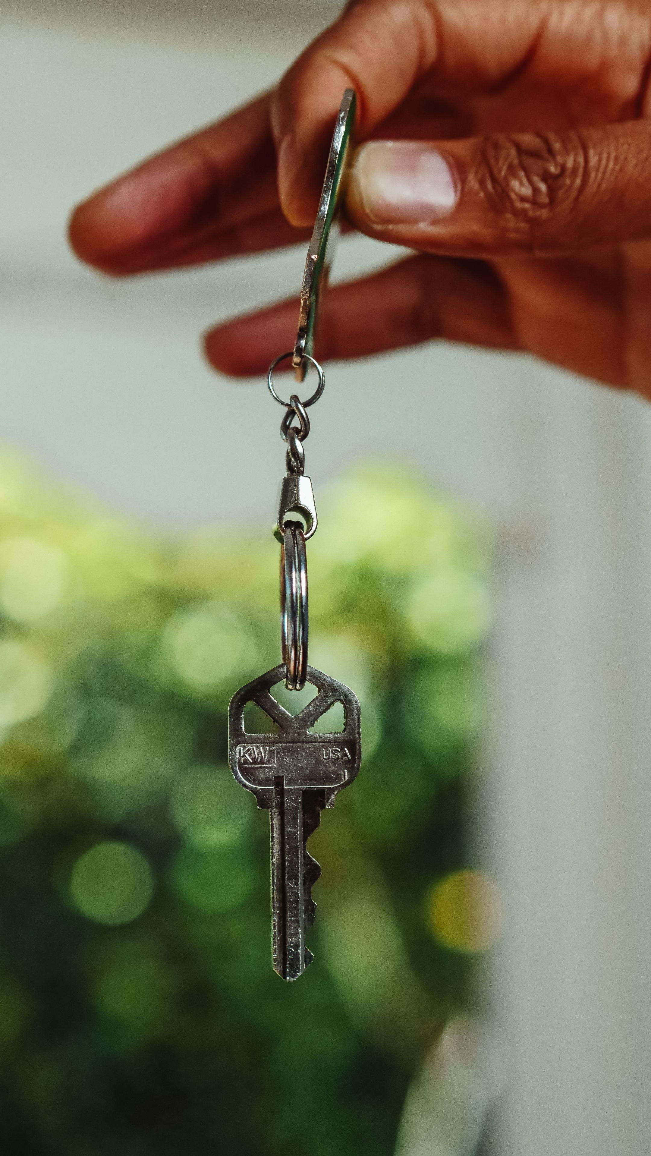 A close-up shot of a hand holding a house key, signifying new home ownership.
