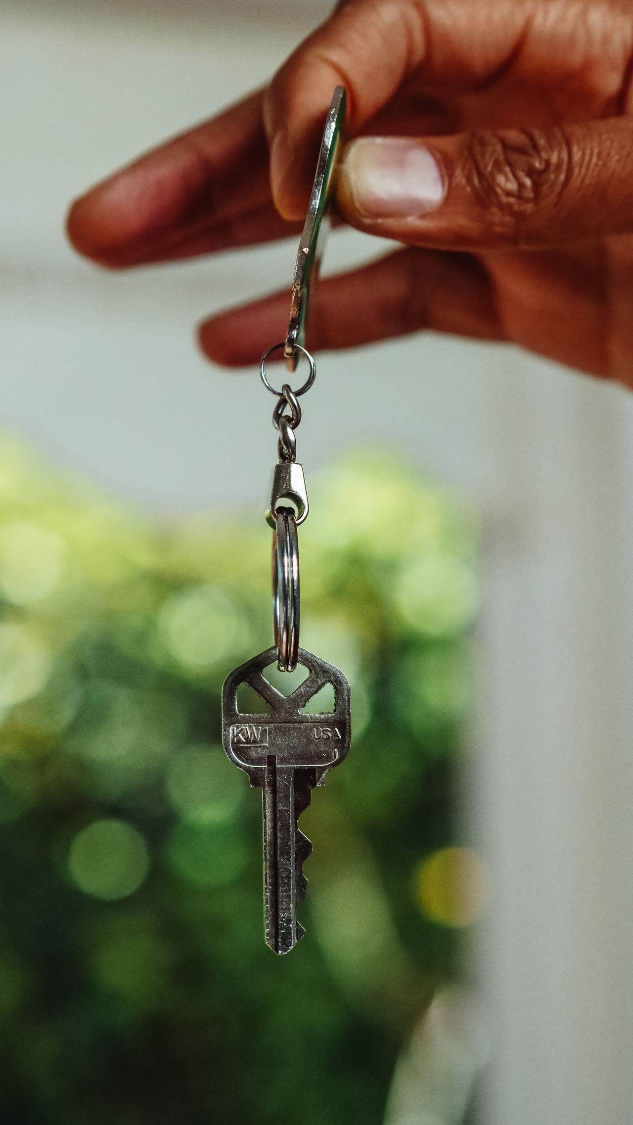 A close-up shot of a hand holding a house key, signifying new home ownership.