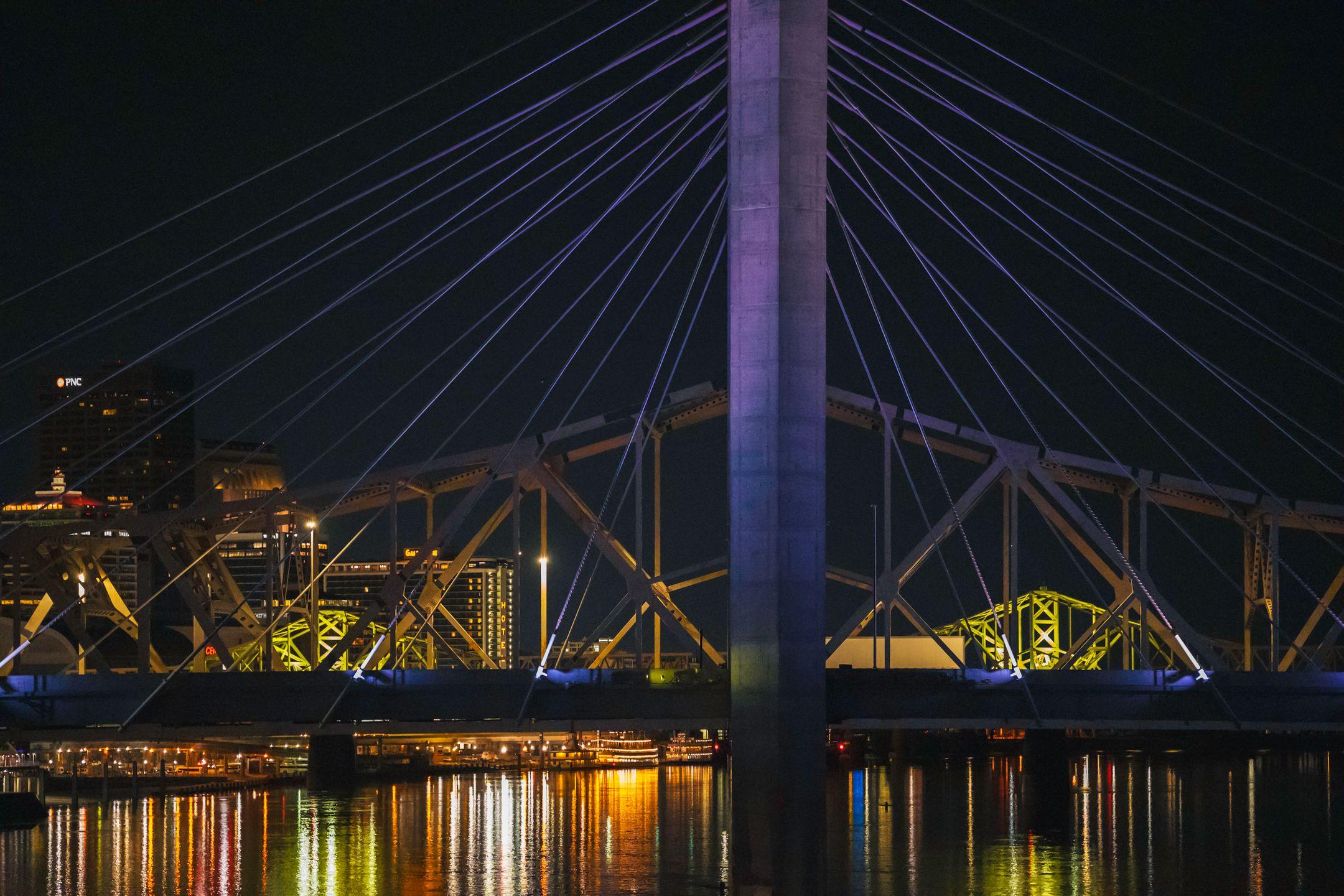 A vibrant night scene of a cable-stayed bridge in Kentucky with city lights reflecting on the water.