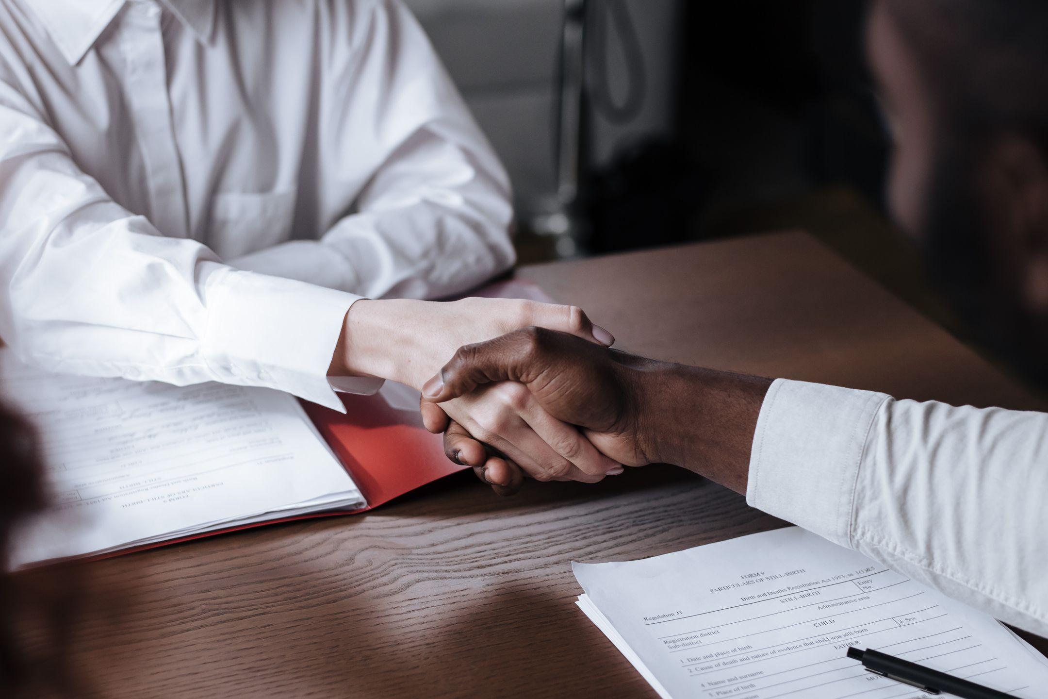 Close-up of a diverse business handshake over documents, symbolizing agreement and collaboration.