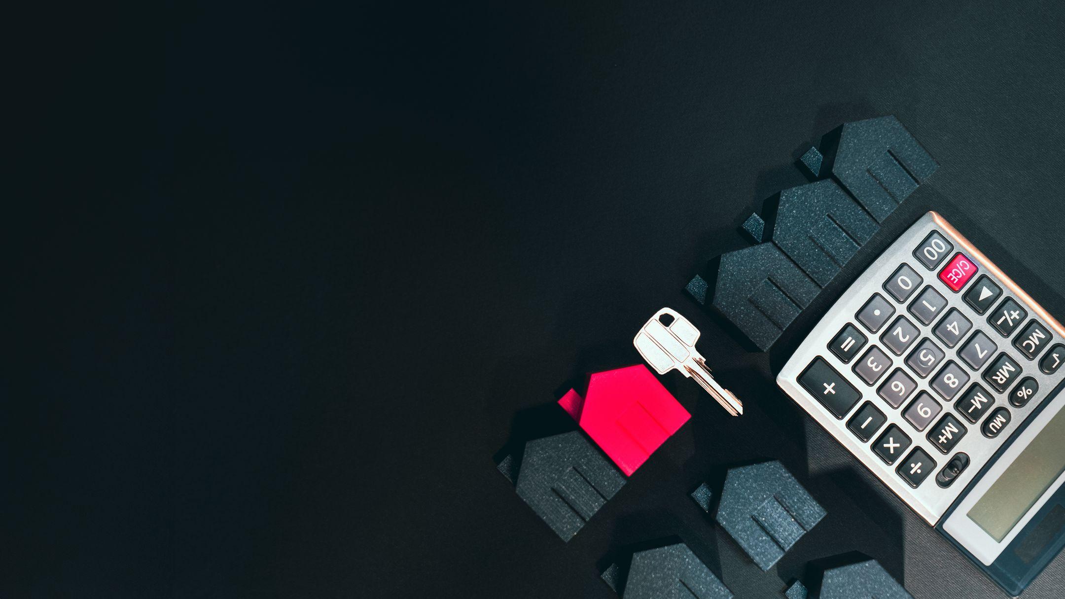 Real estate concept image featuring a calculator, houses, and a key on a black background.