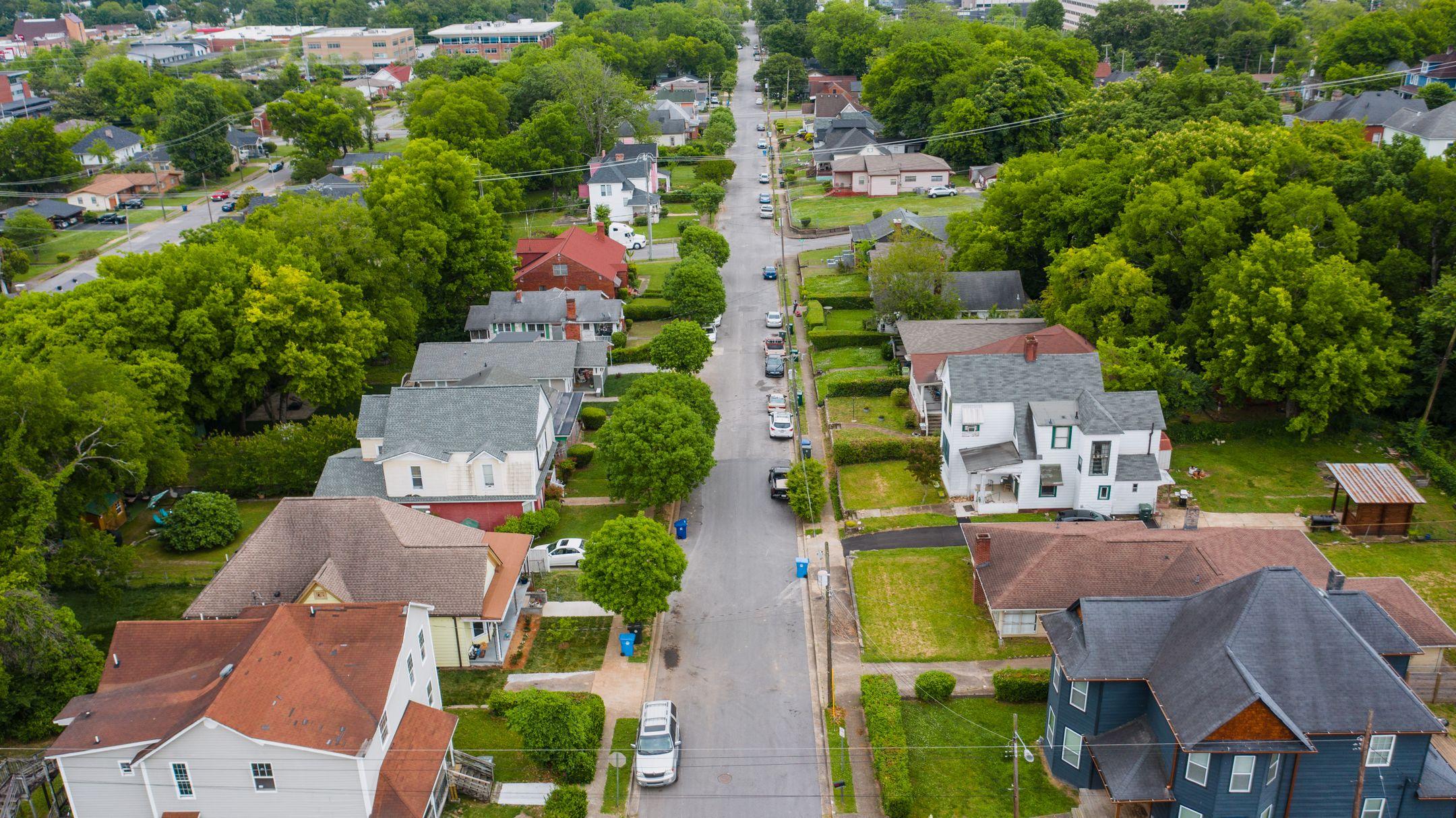 Drone shot showcasing a charming residential area with houses, trees, and parked vehicles.