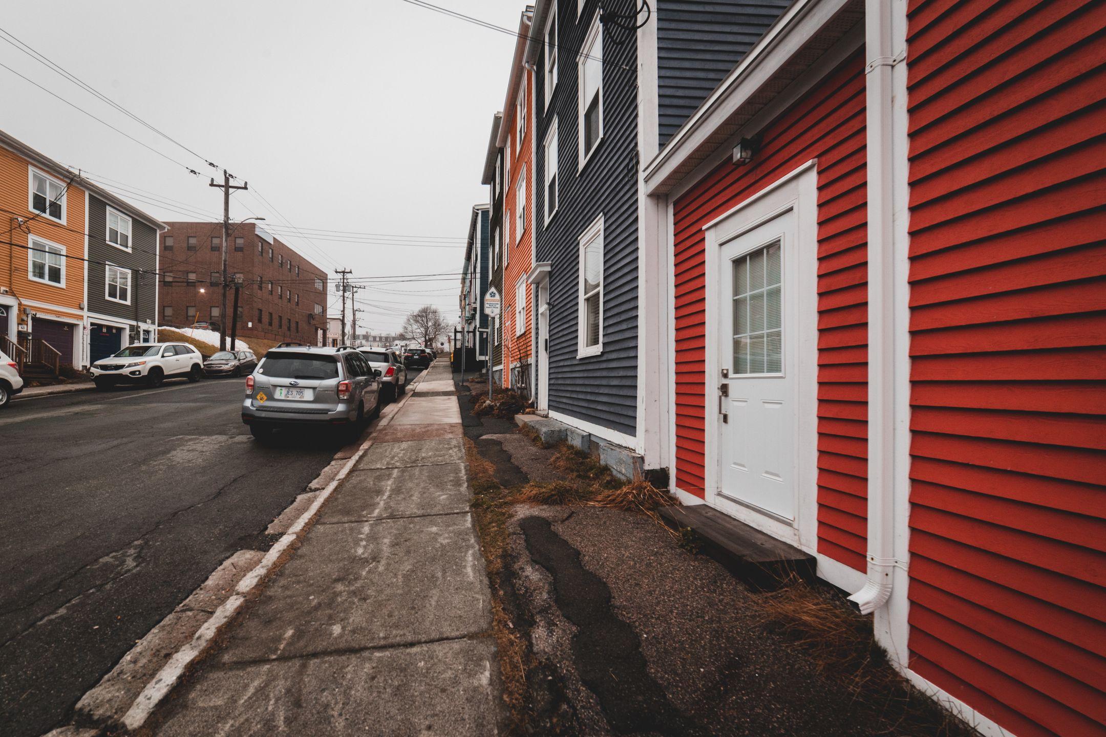 Bright old fashioned residential houses with windows located near asphalt roadway with modern cars on street of town against cloudless sky