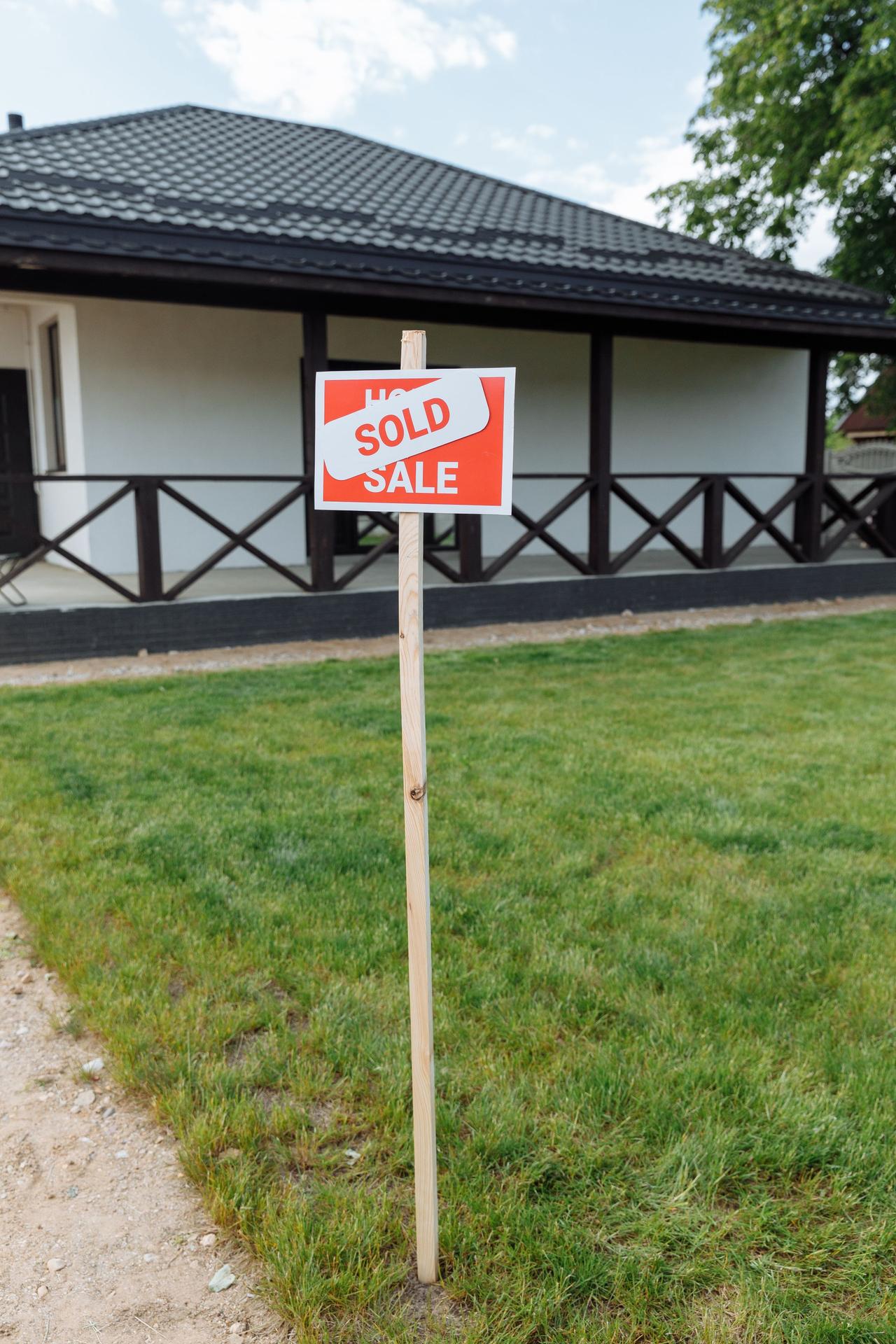 A modern house with a sold sign on a grassy lawn, indicating property purchase.