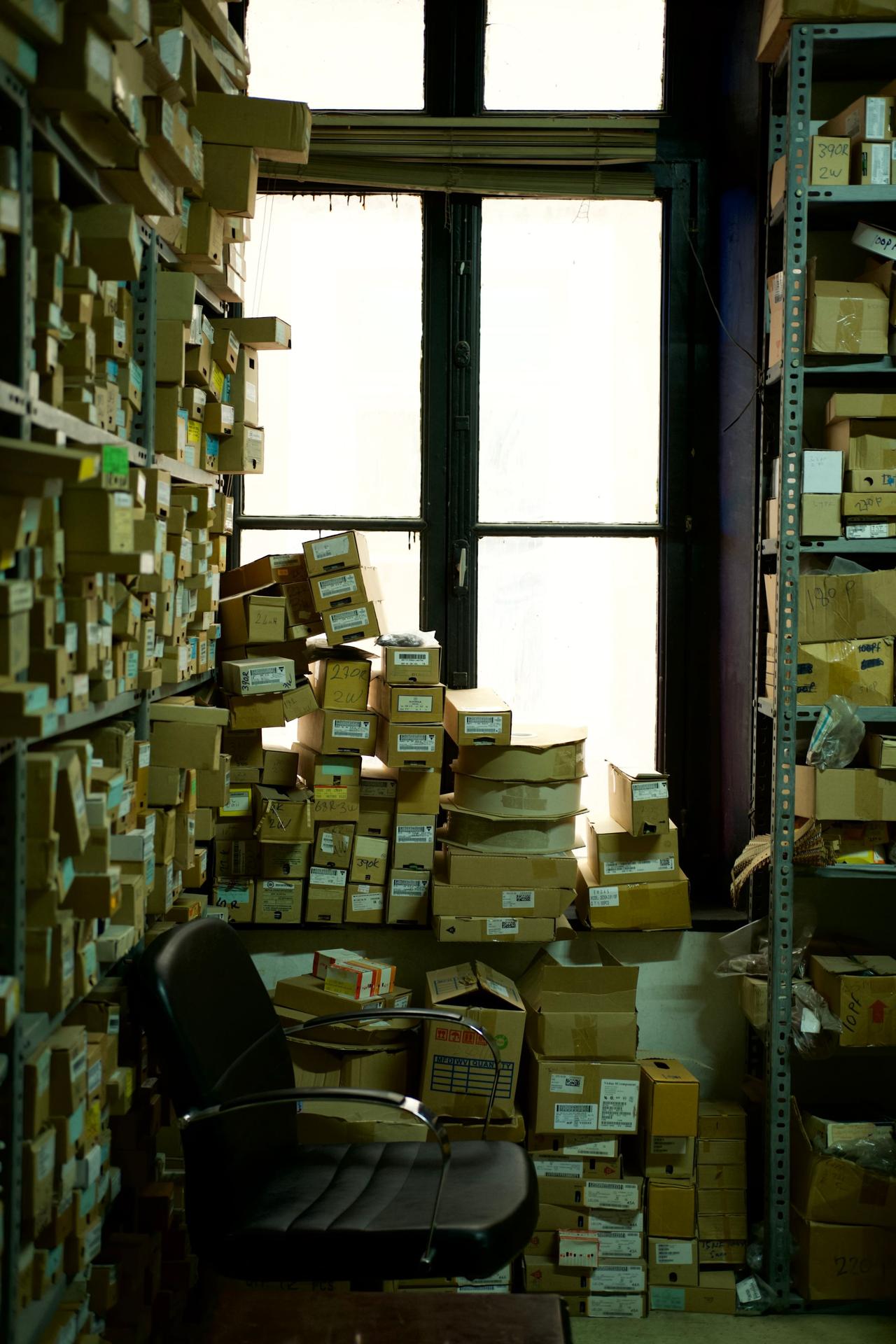 A cluttered storage room filled with cardboard boxes and an office chair by a window.