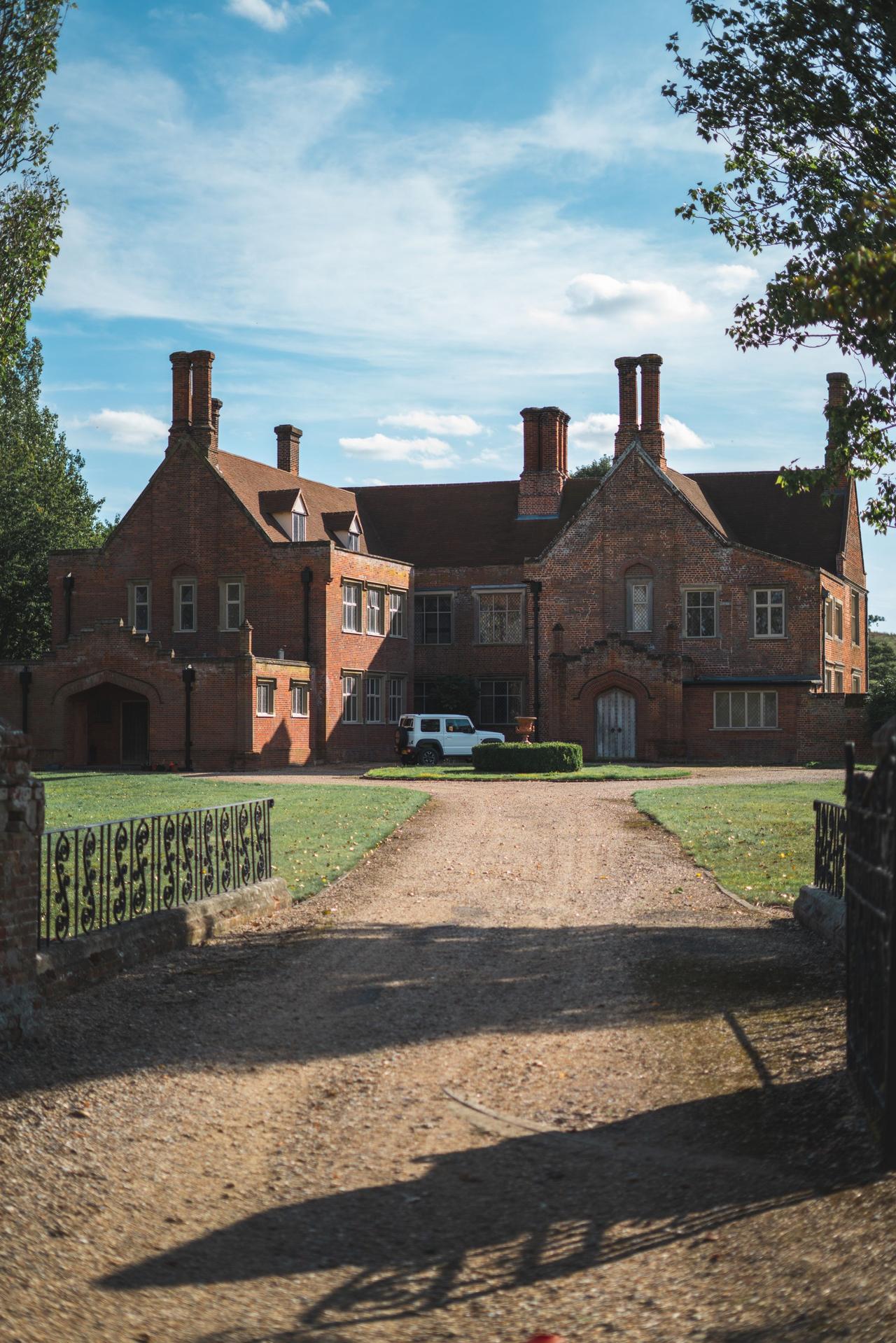 An elegant brick mansion with a large driveway and surrounding lawn under a clear sky.