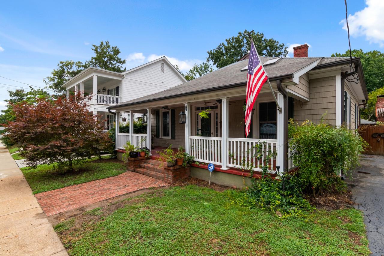 Quaint American bungalow with flag and lush garden under a blue sky.