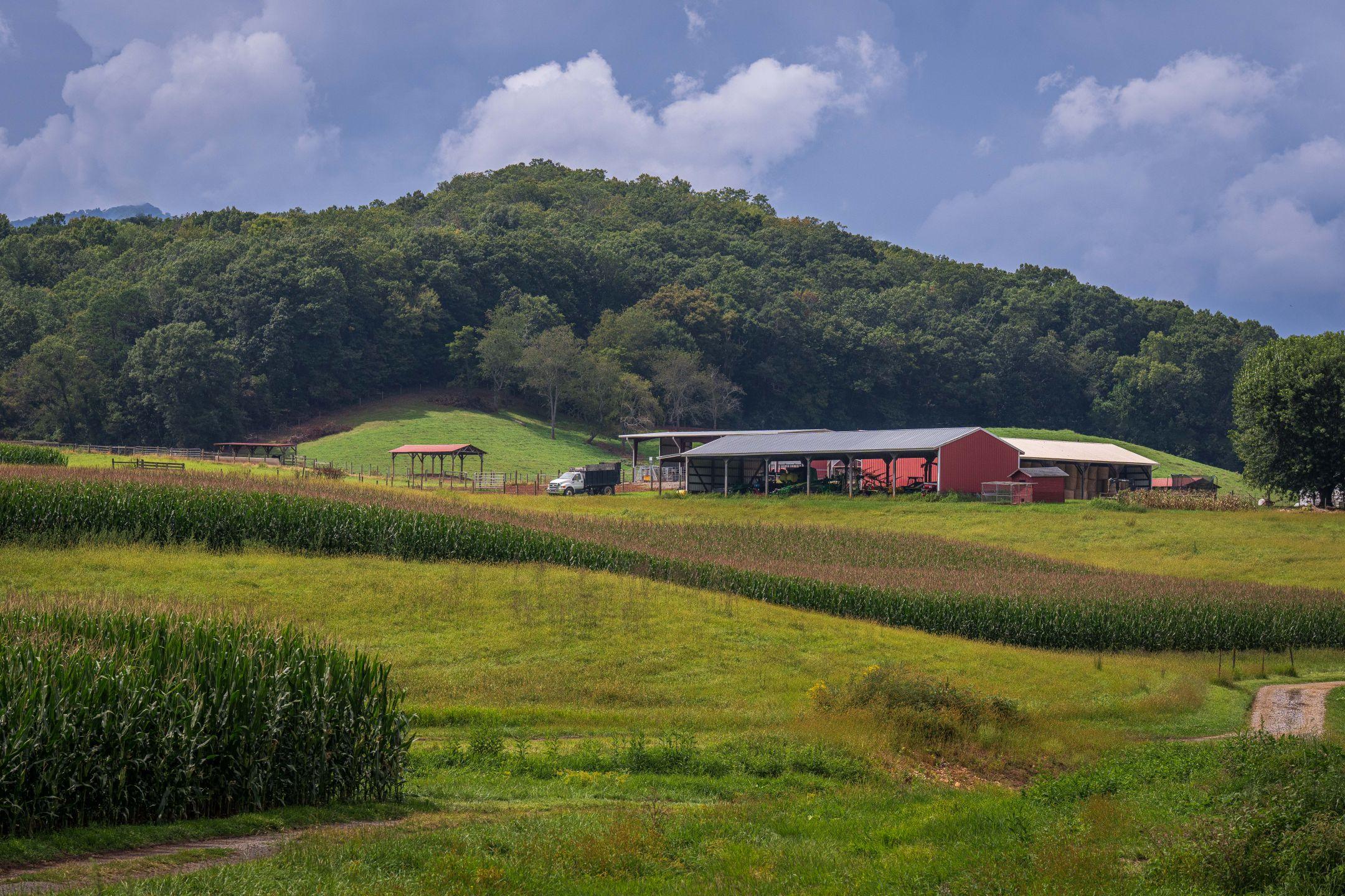 Scenic view of a countryside farm with a red barn, lush fields, and hills under a cloudy sky.