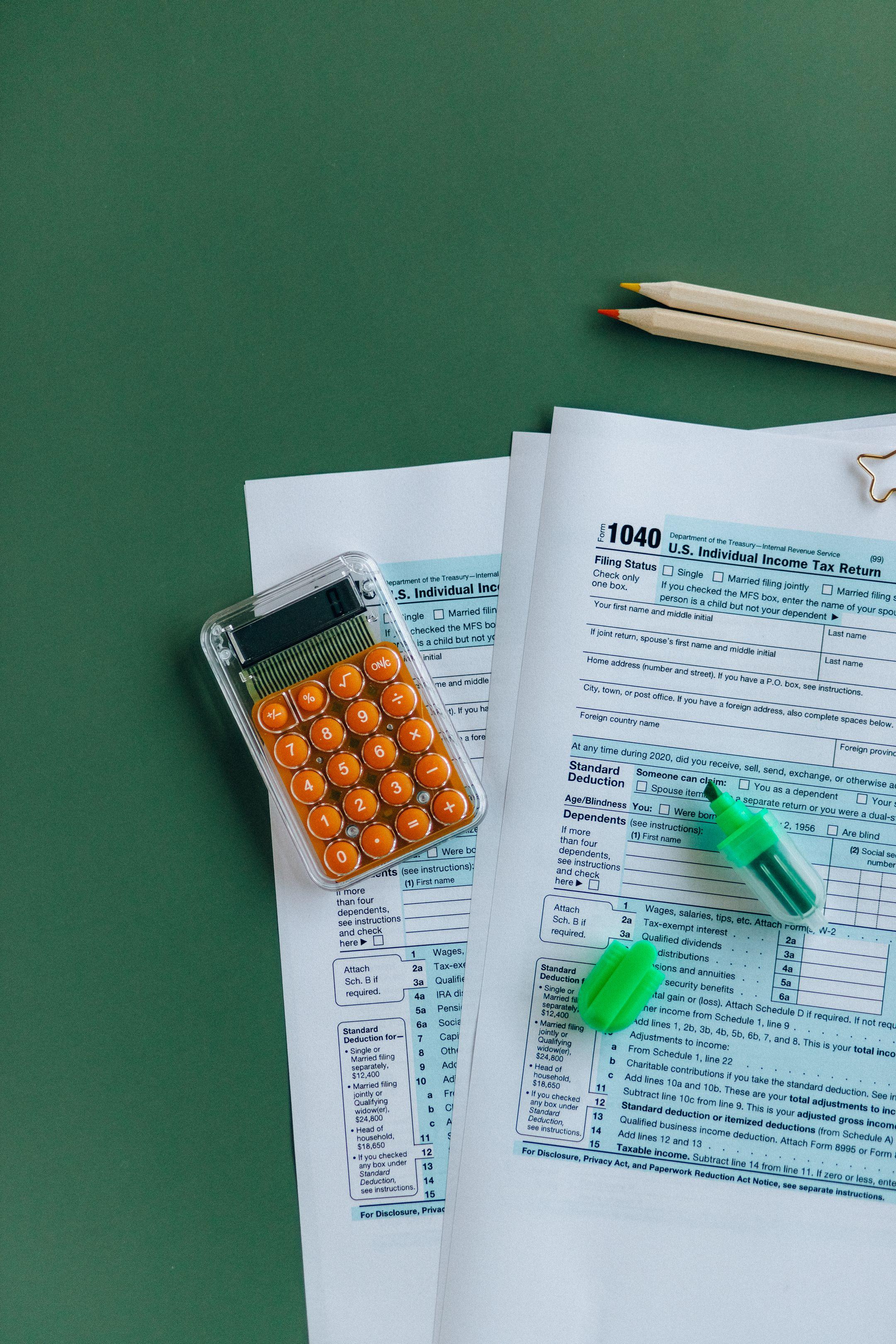 1040 tax forms with calculator, pencils, and markers on green surface.