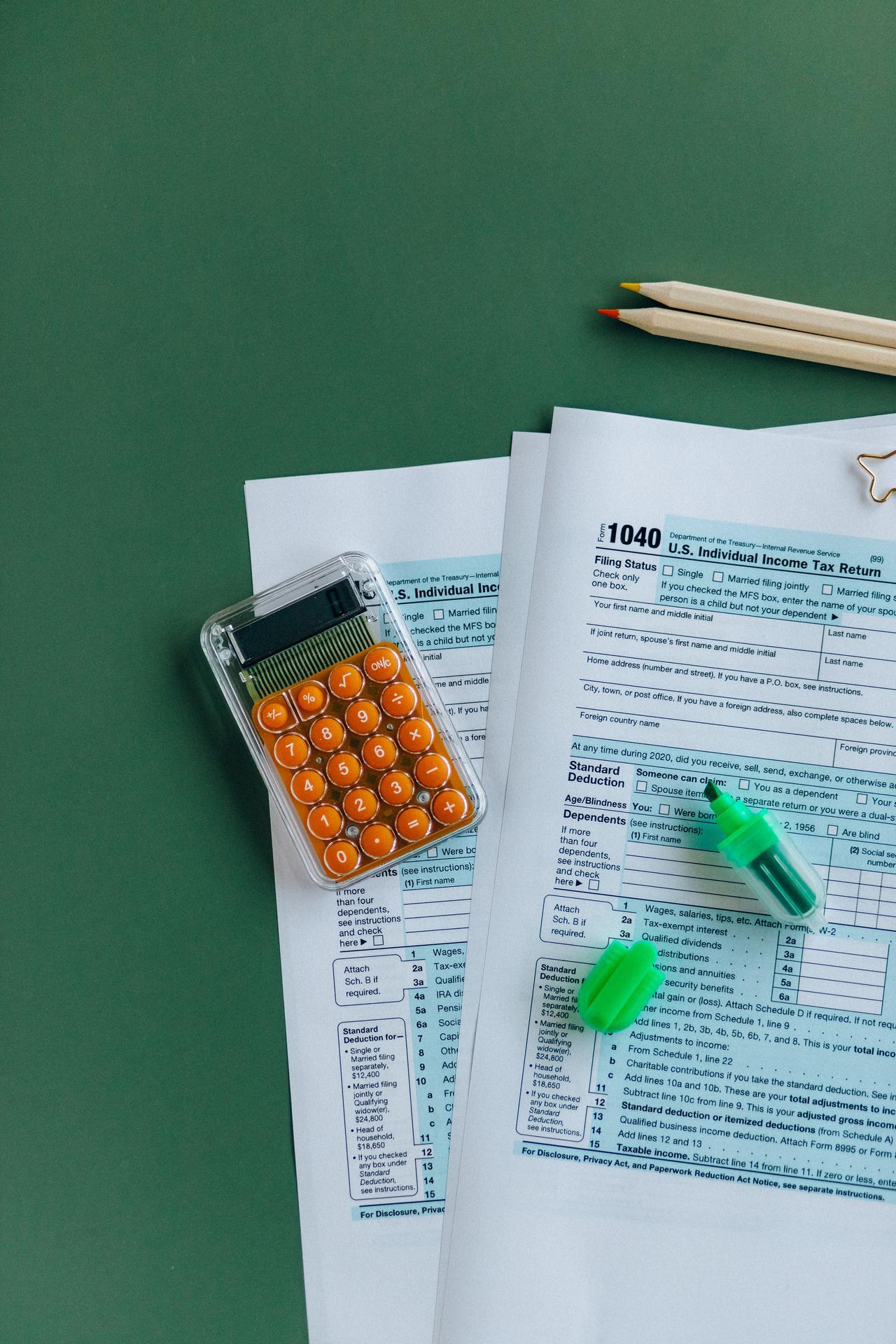 1040 tax forms with calculator, pencils, and markers on green surface.