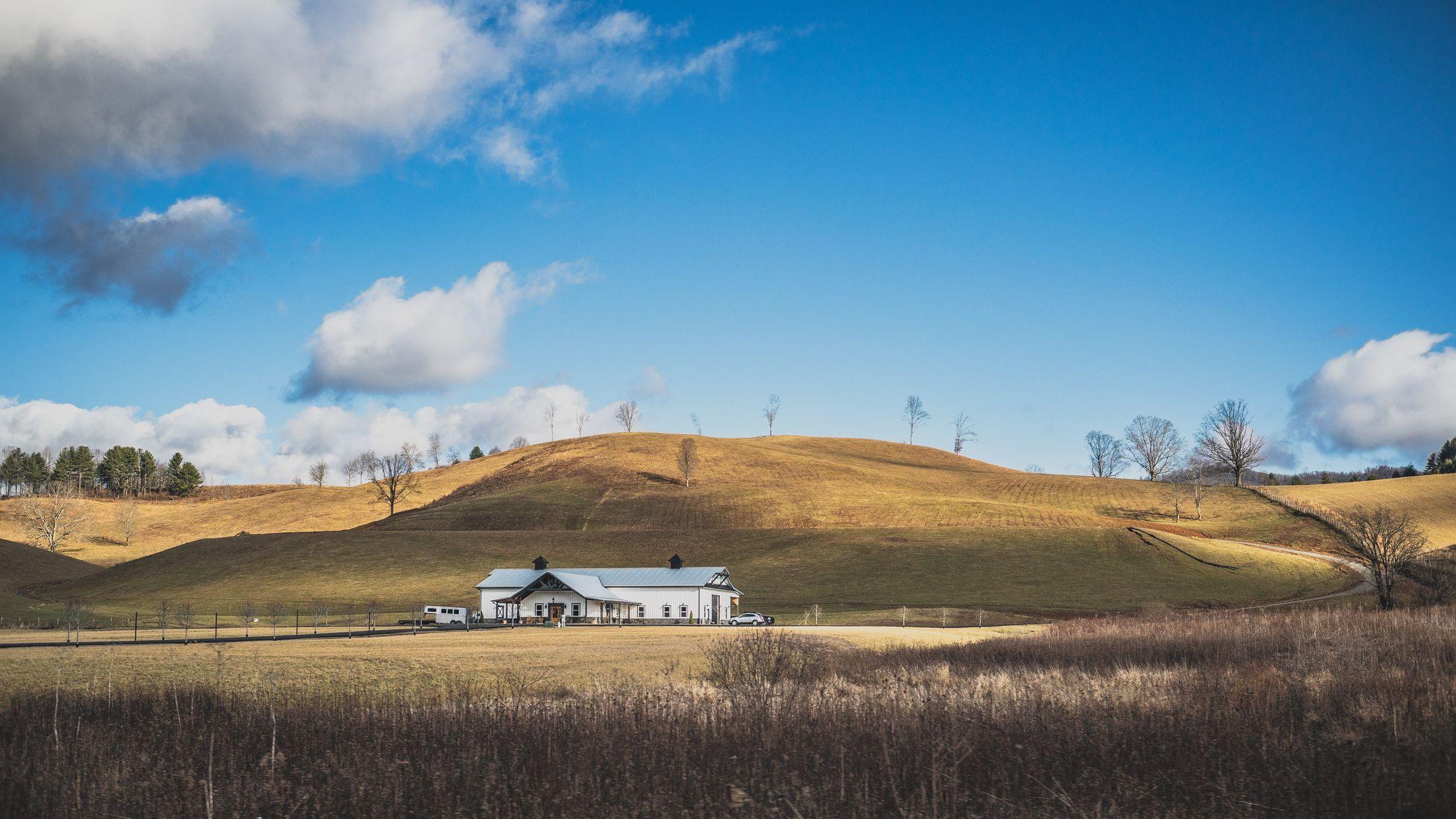 Charming farmhouse nestled in scenic rolling hills under a bright sky.