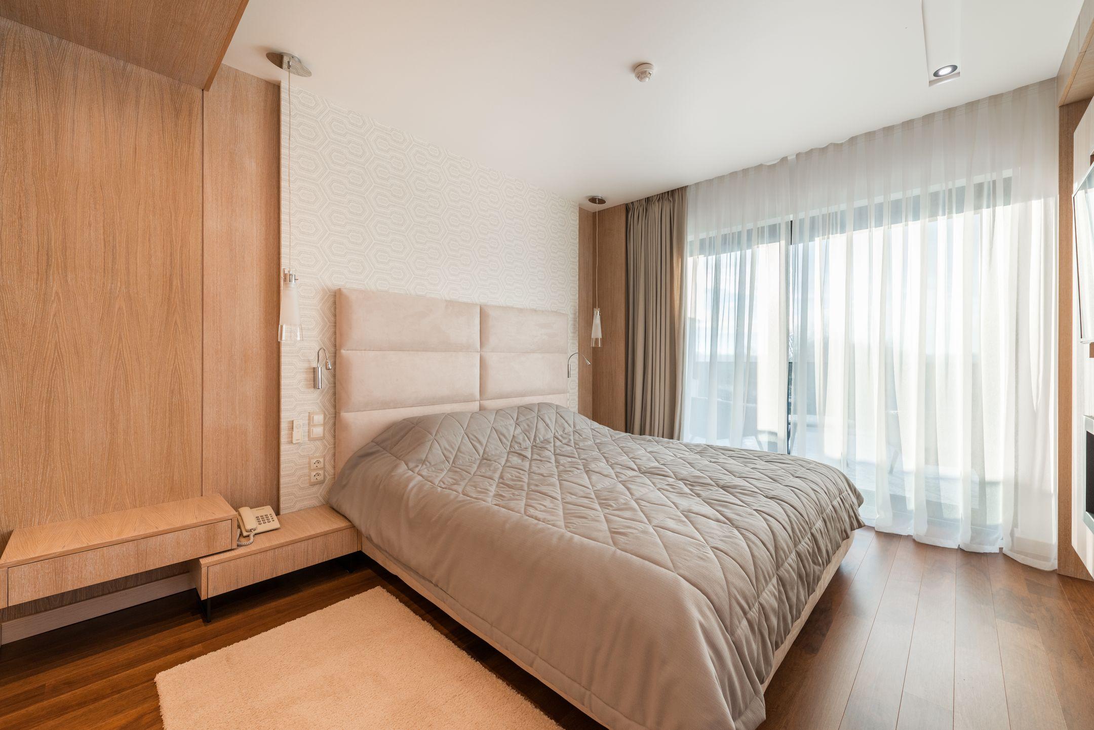 Comfortable bed with blanket placed at wall near window with curtains in modern stylish bedroom with wooden wardrobe with telephone