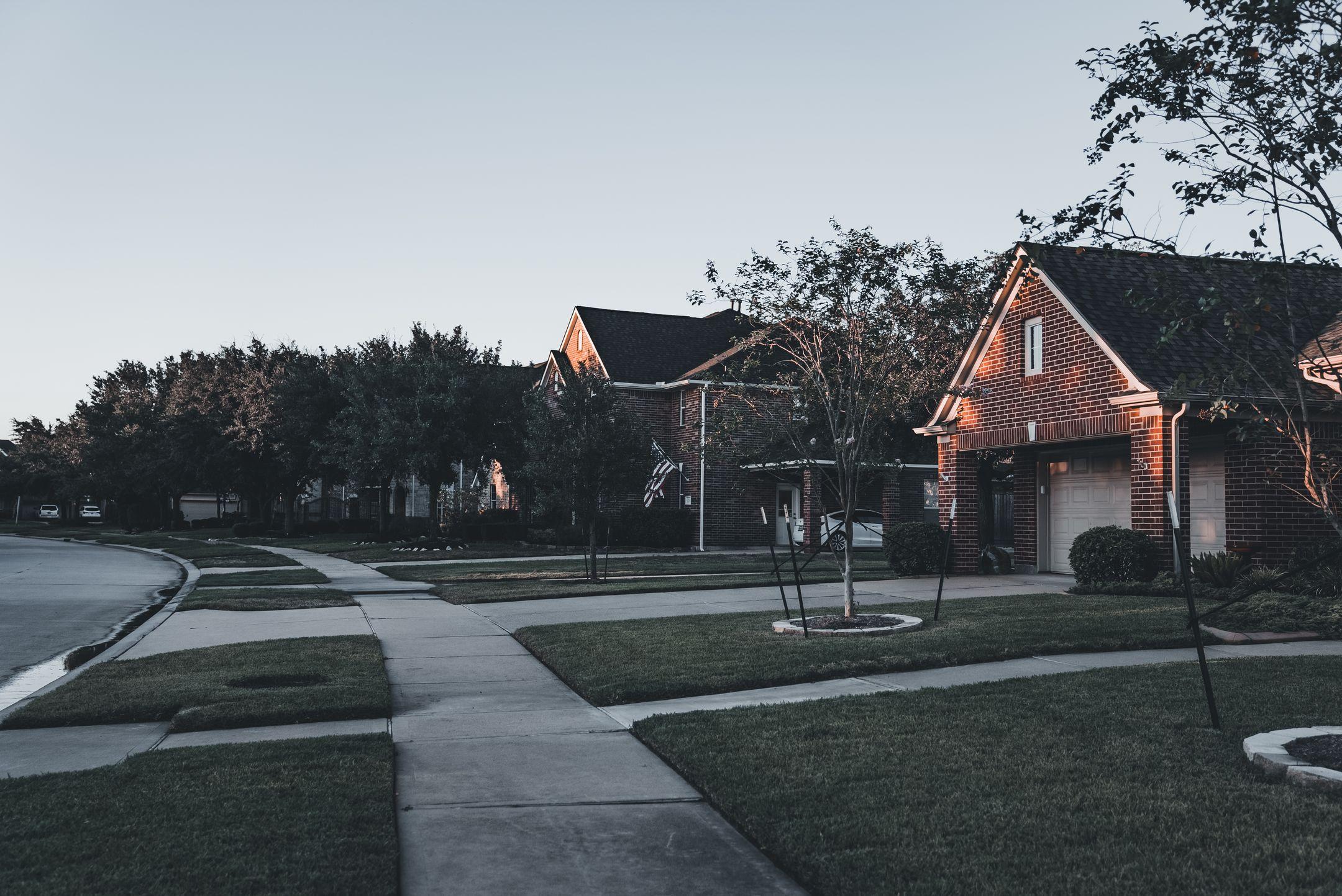 A serene suburban scene featuring brick houses and landscaped lawns at dusk.