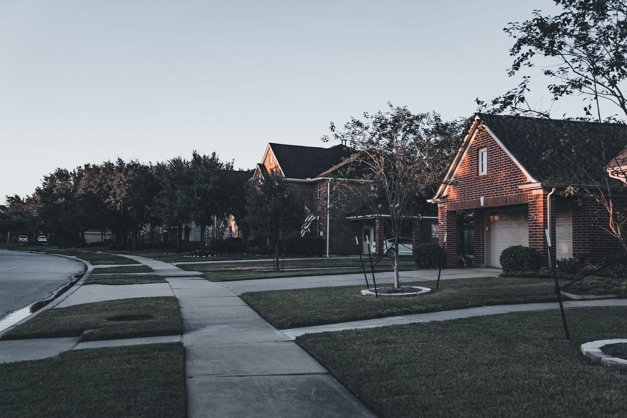 A serene suburban scene featuring brick houses and landscaped lawns at dusk.