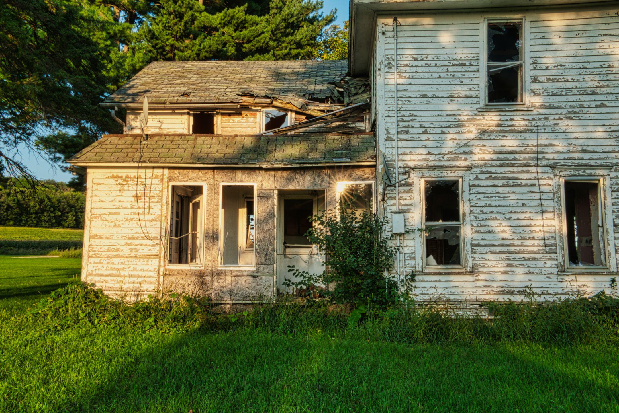 Old, decaying wooden house set in a lush green field, captured at sunset.