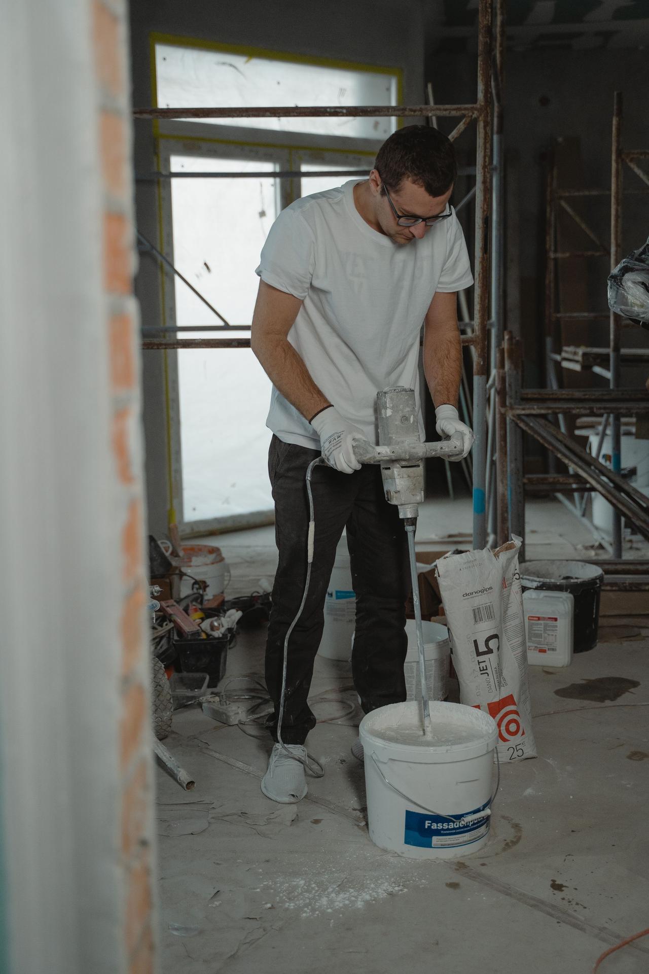 Male construction worker using a mixer to prepare plaster indoors.