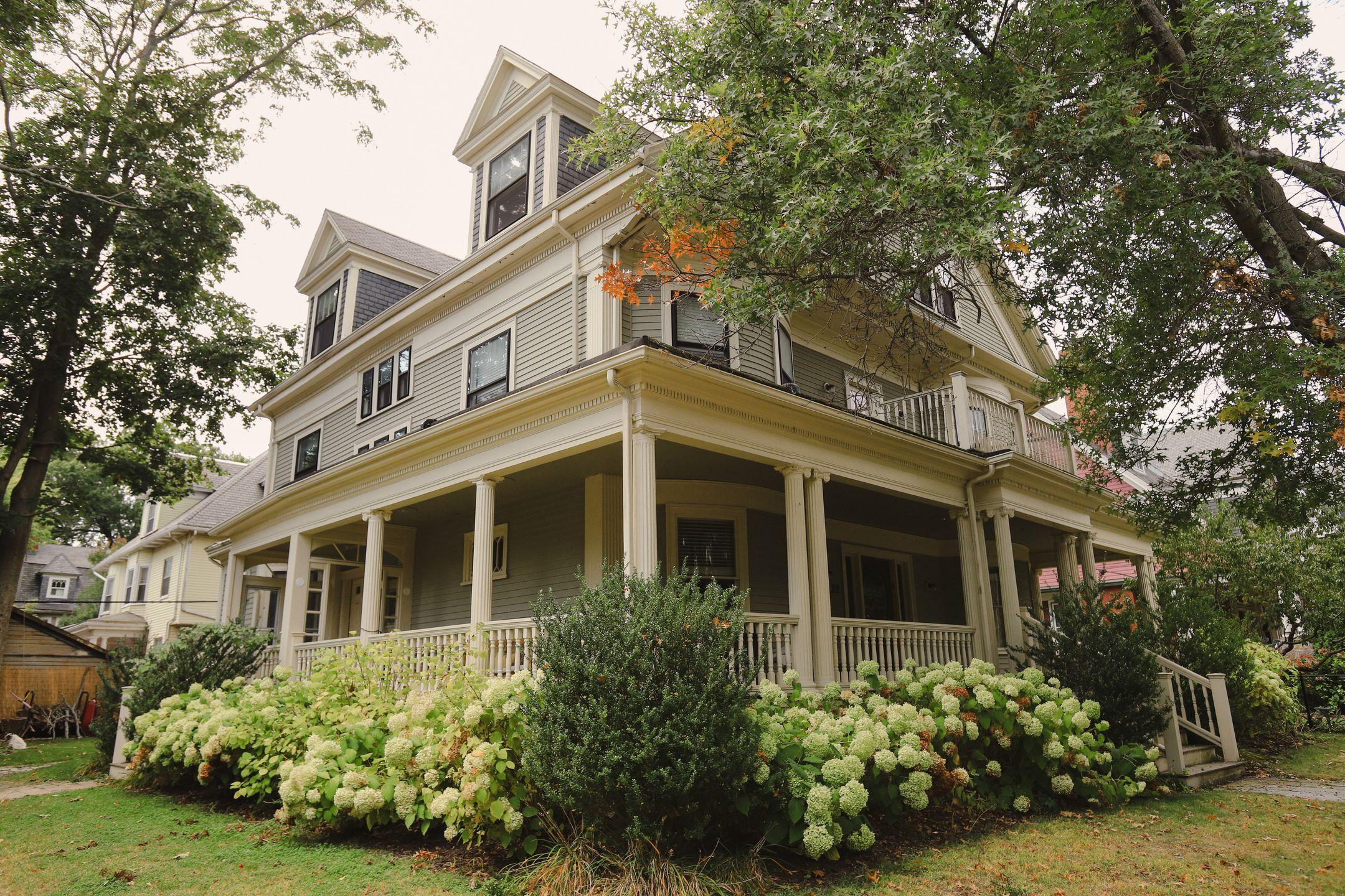 Charming traditional house with a wraparound porch, surrounded by lush garden.