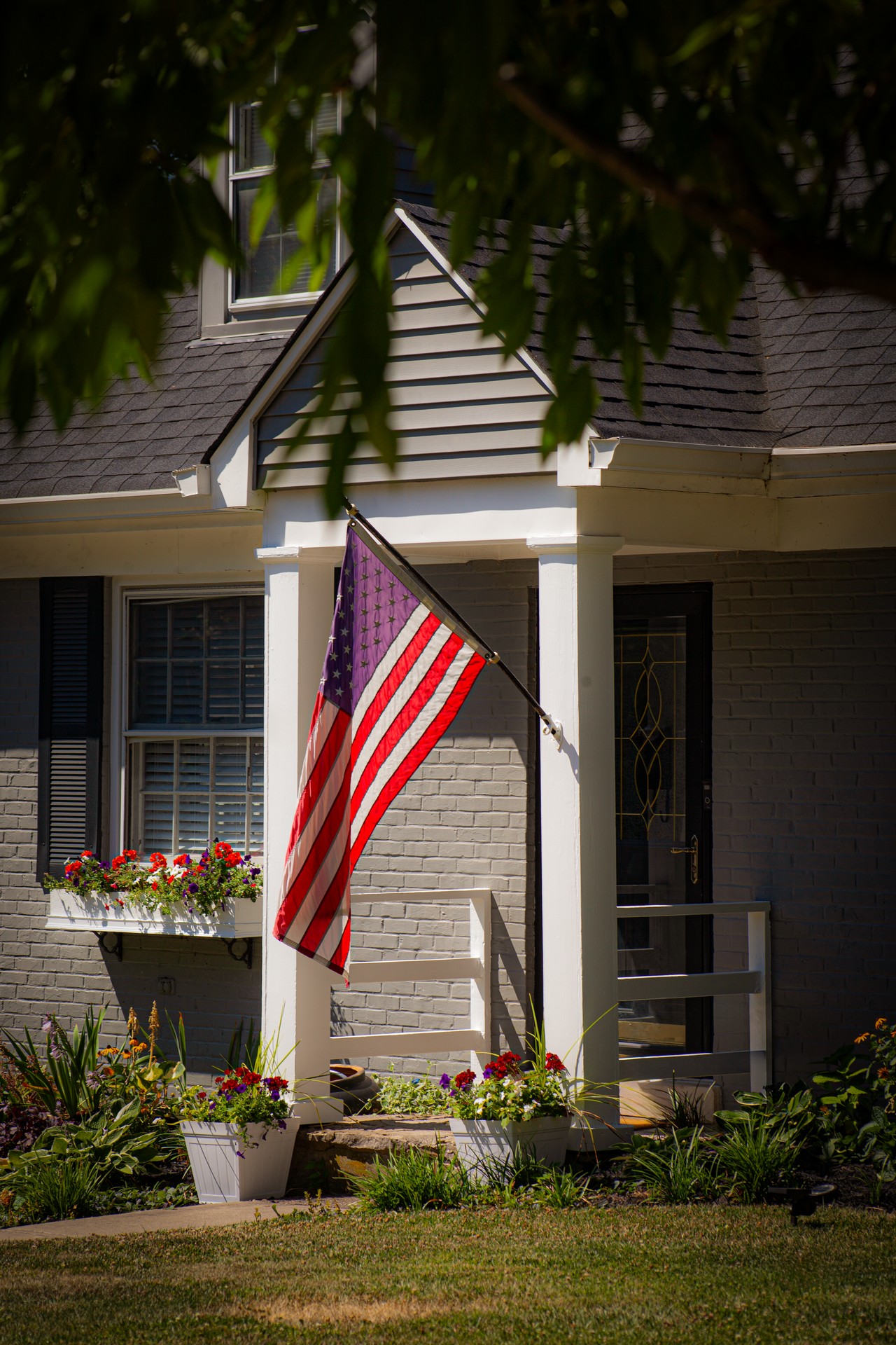 A suburban house entrance with a prominently displayed American flag and vibrant flowers.