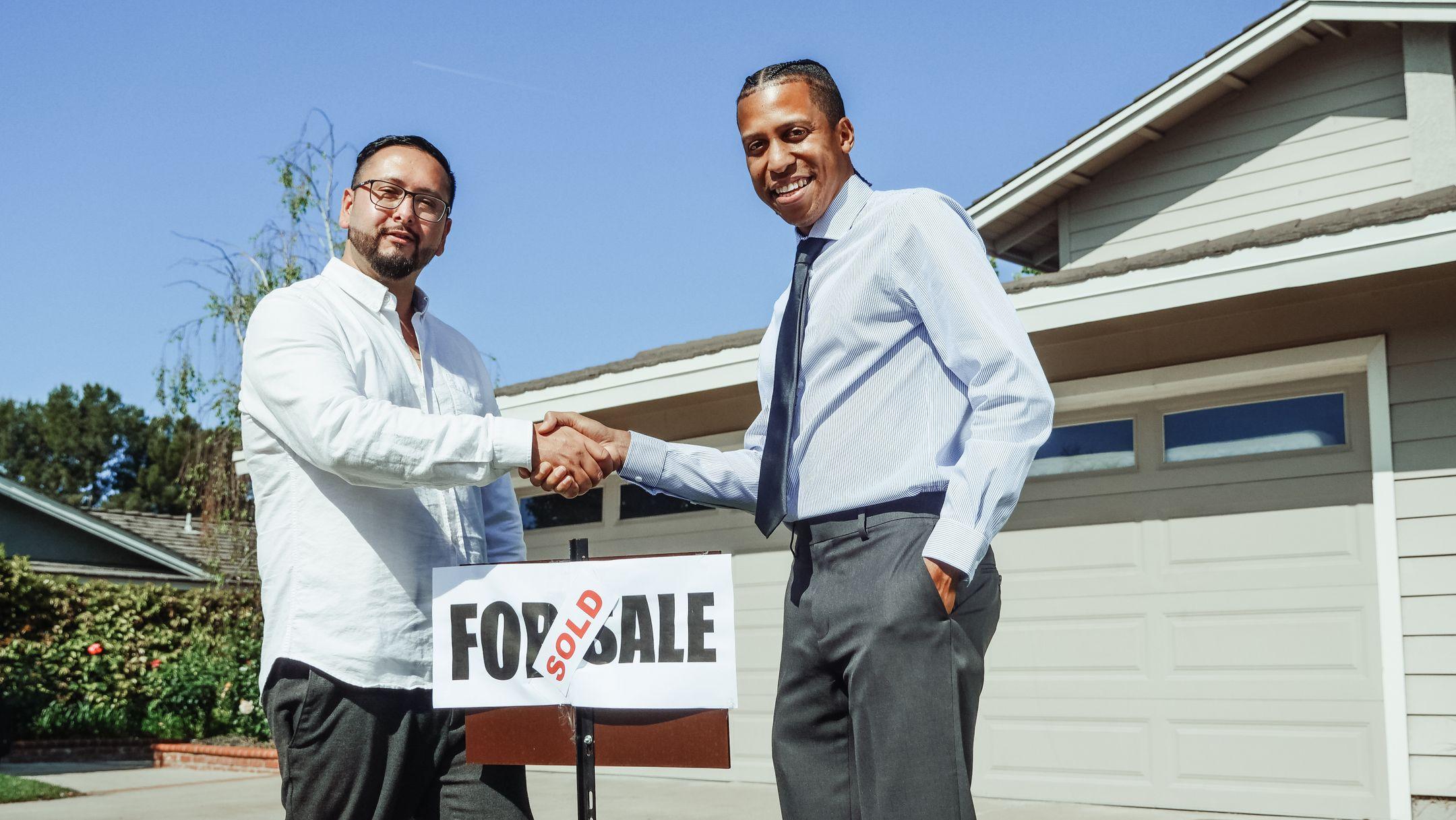 Two men shaking hands in front of a sold house, symbolizing a successful real estate transaction.
